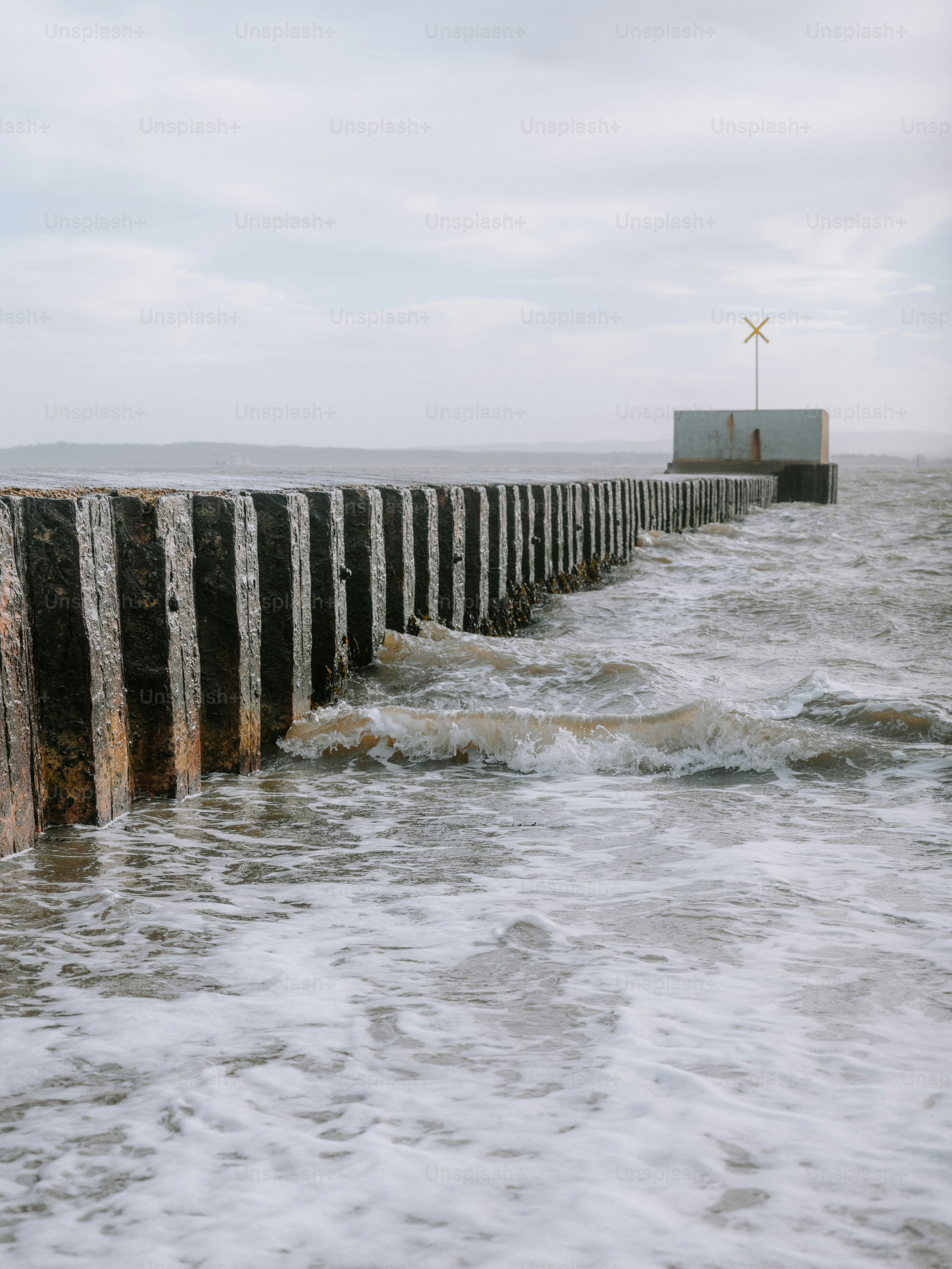 Waves crash against a wooden pier with a small structure.