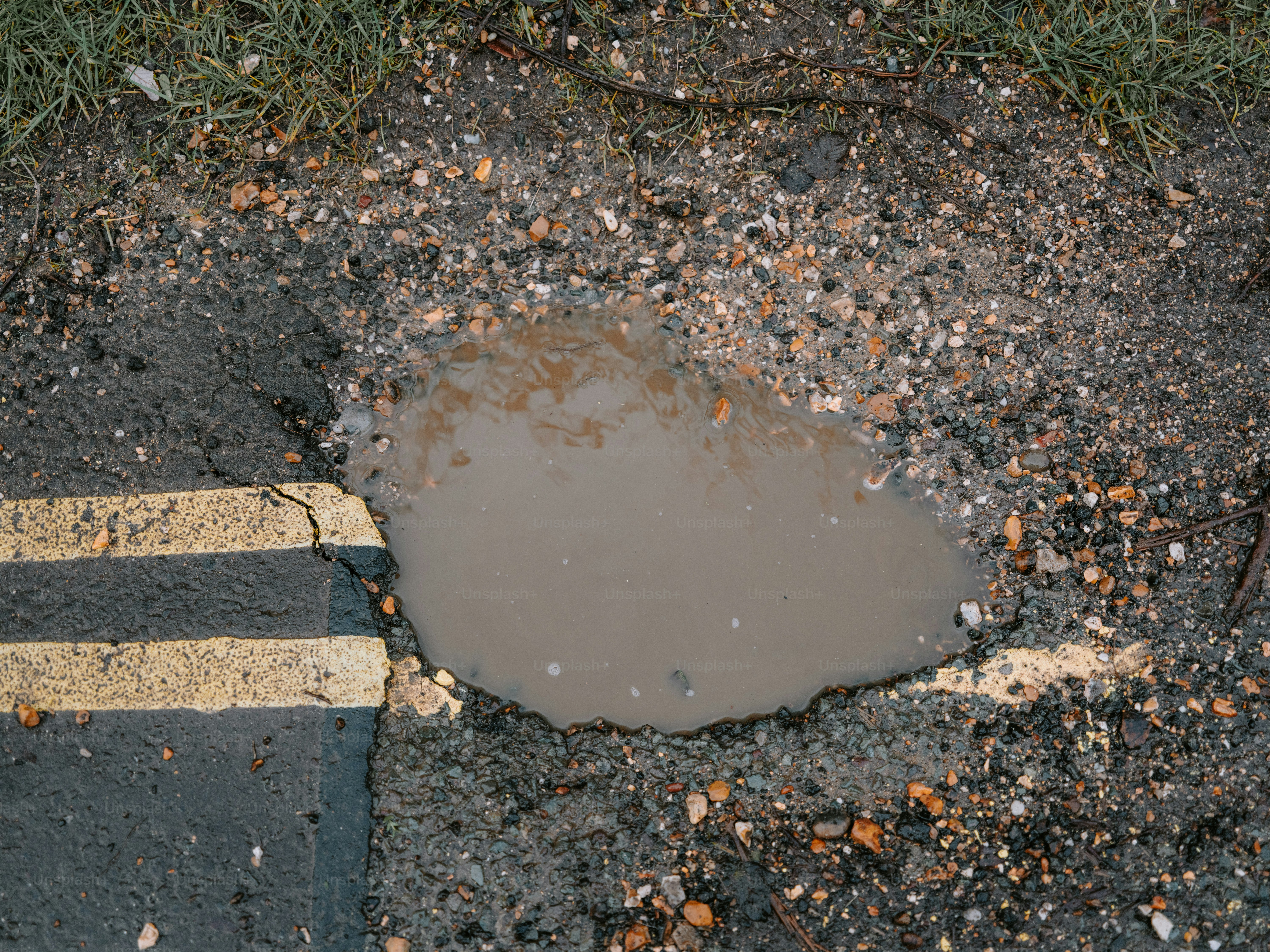A muddy puddle on a damaged asphalt road