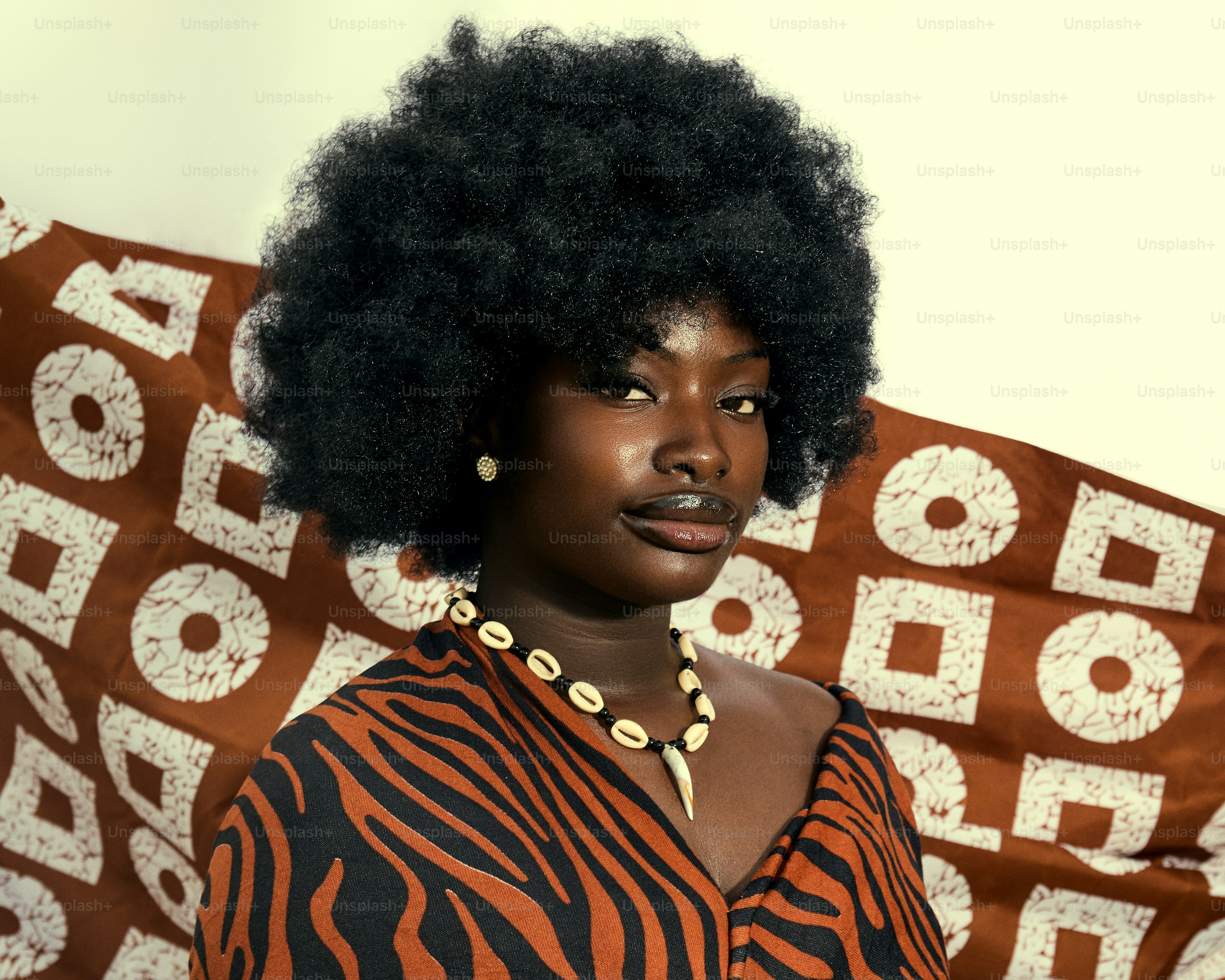 Frau mit Afro- und Muschelhalskette auf gemustertem Stoff