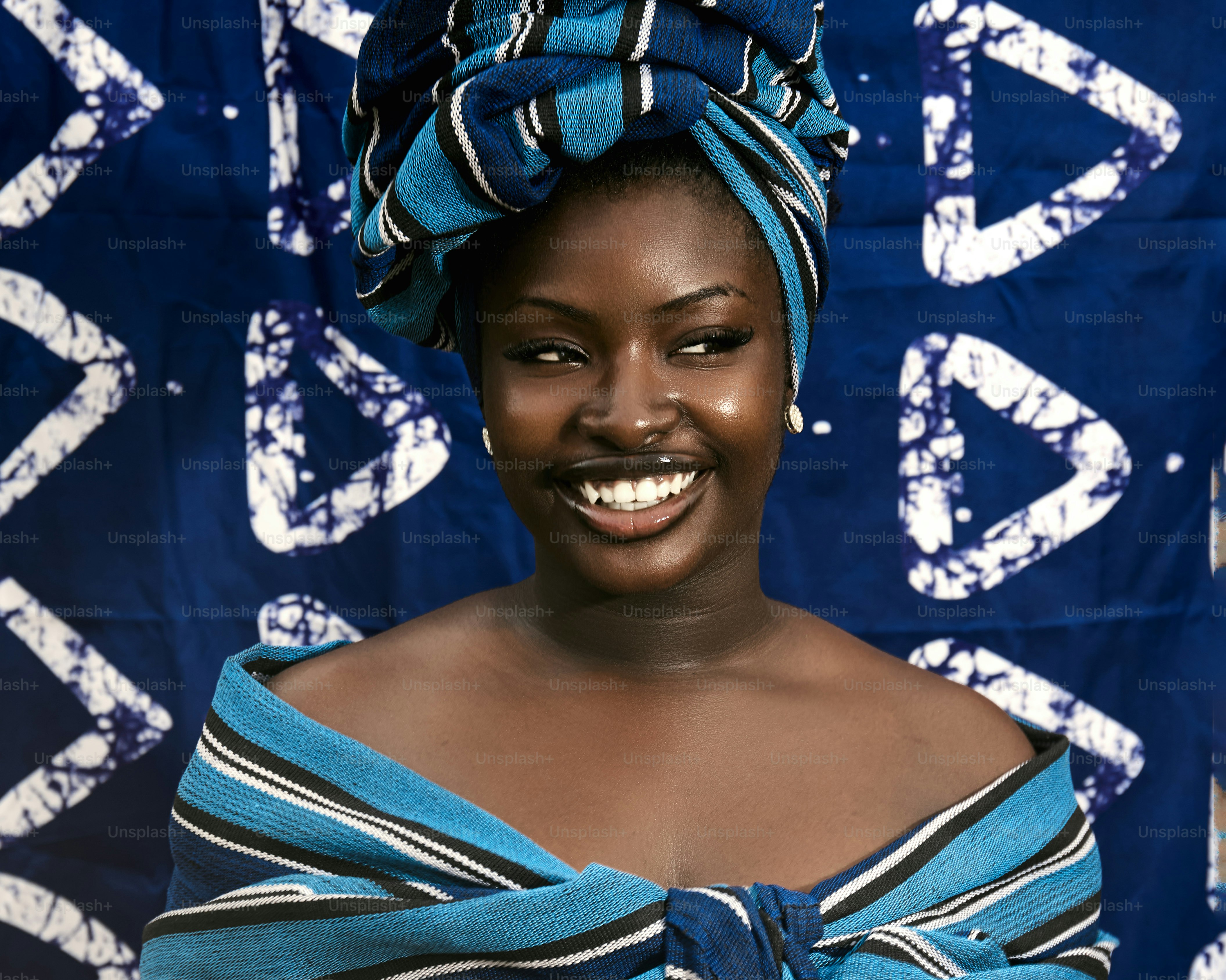 A smiling woman in a blue headwrap and dress