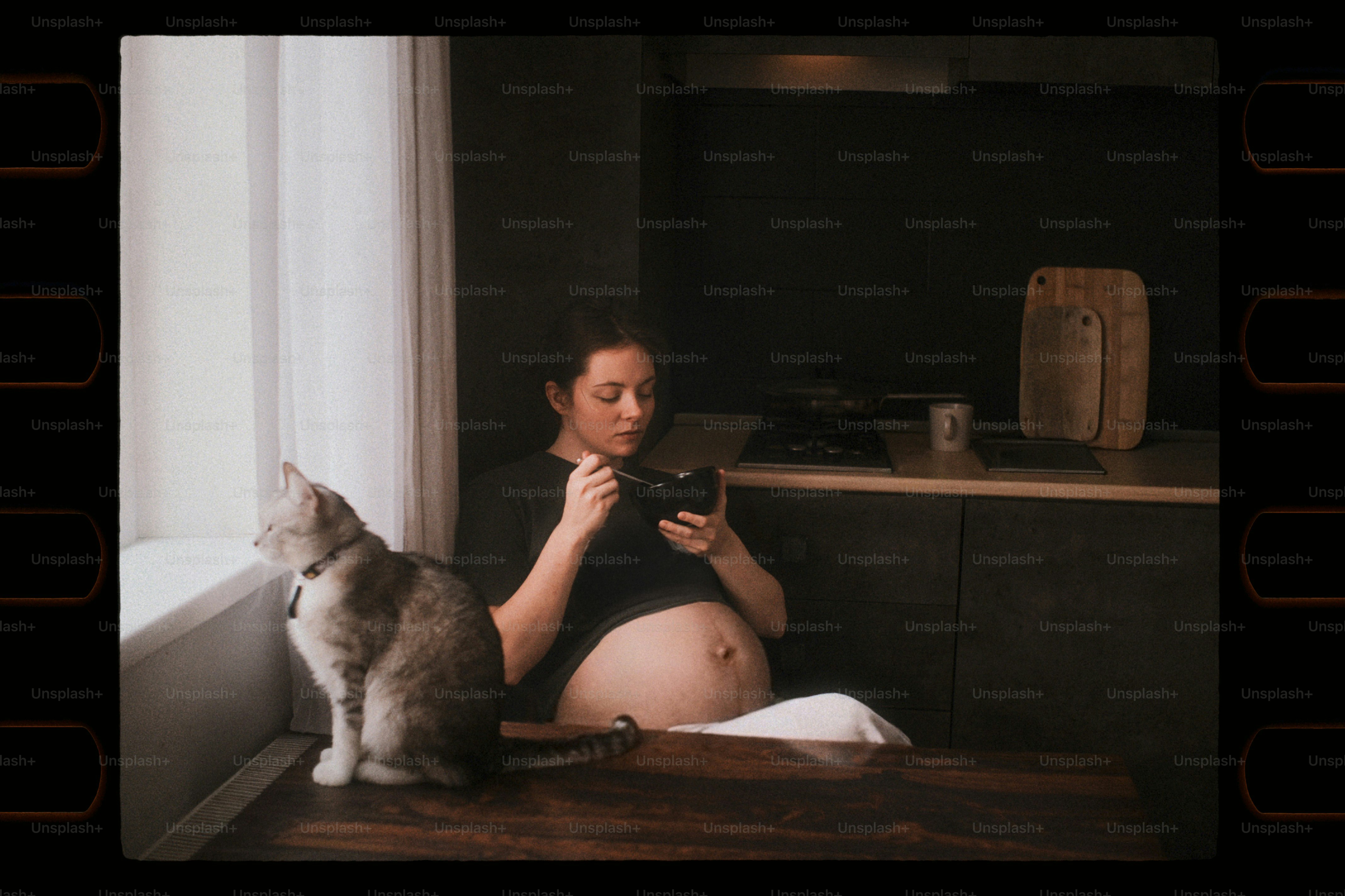 Femme enceinte mangeant avec un chat près de la fenêtre