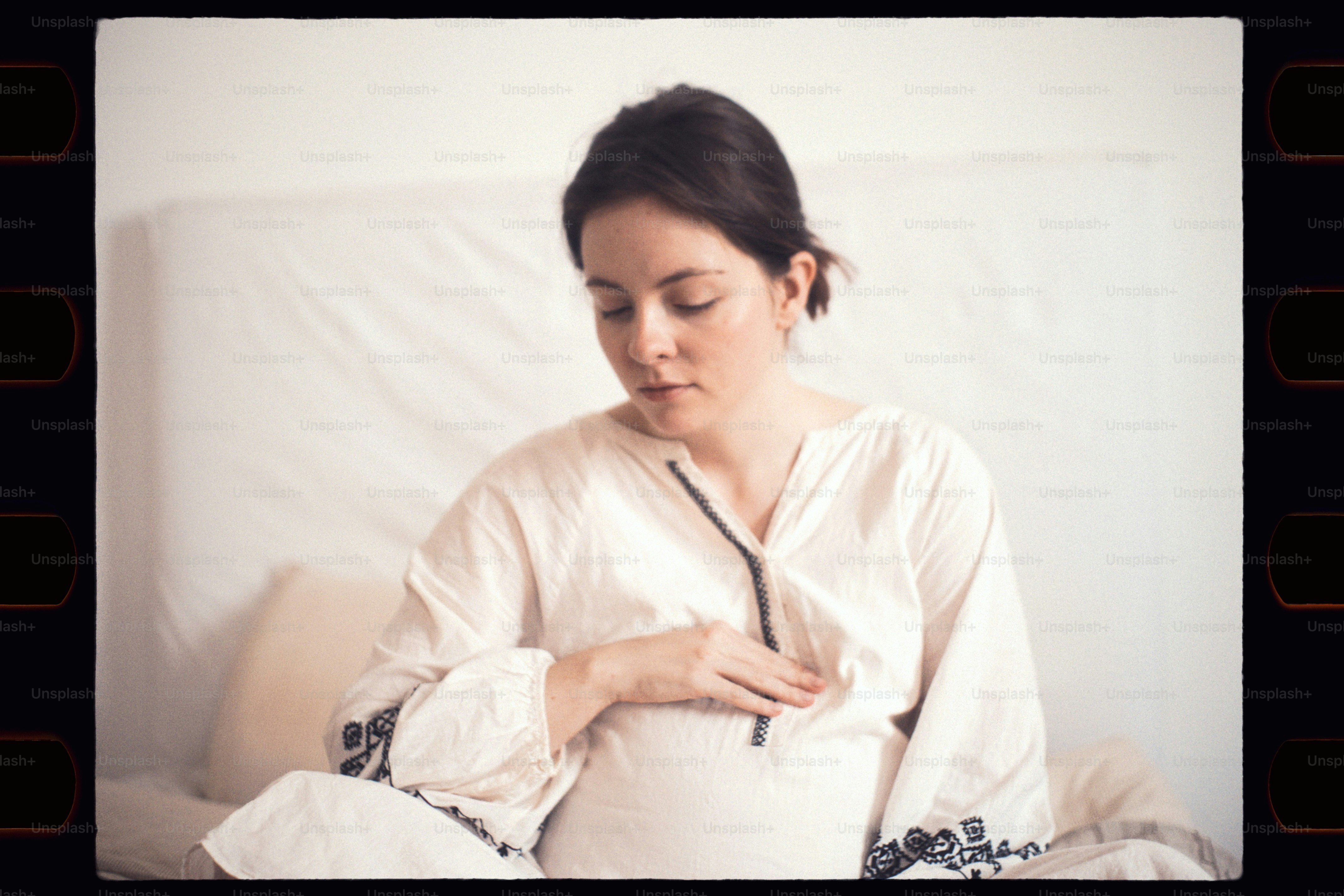 Une femme enceinte en haut blanc repose dans son lit.