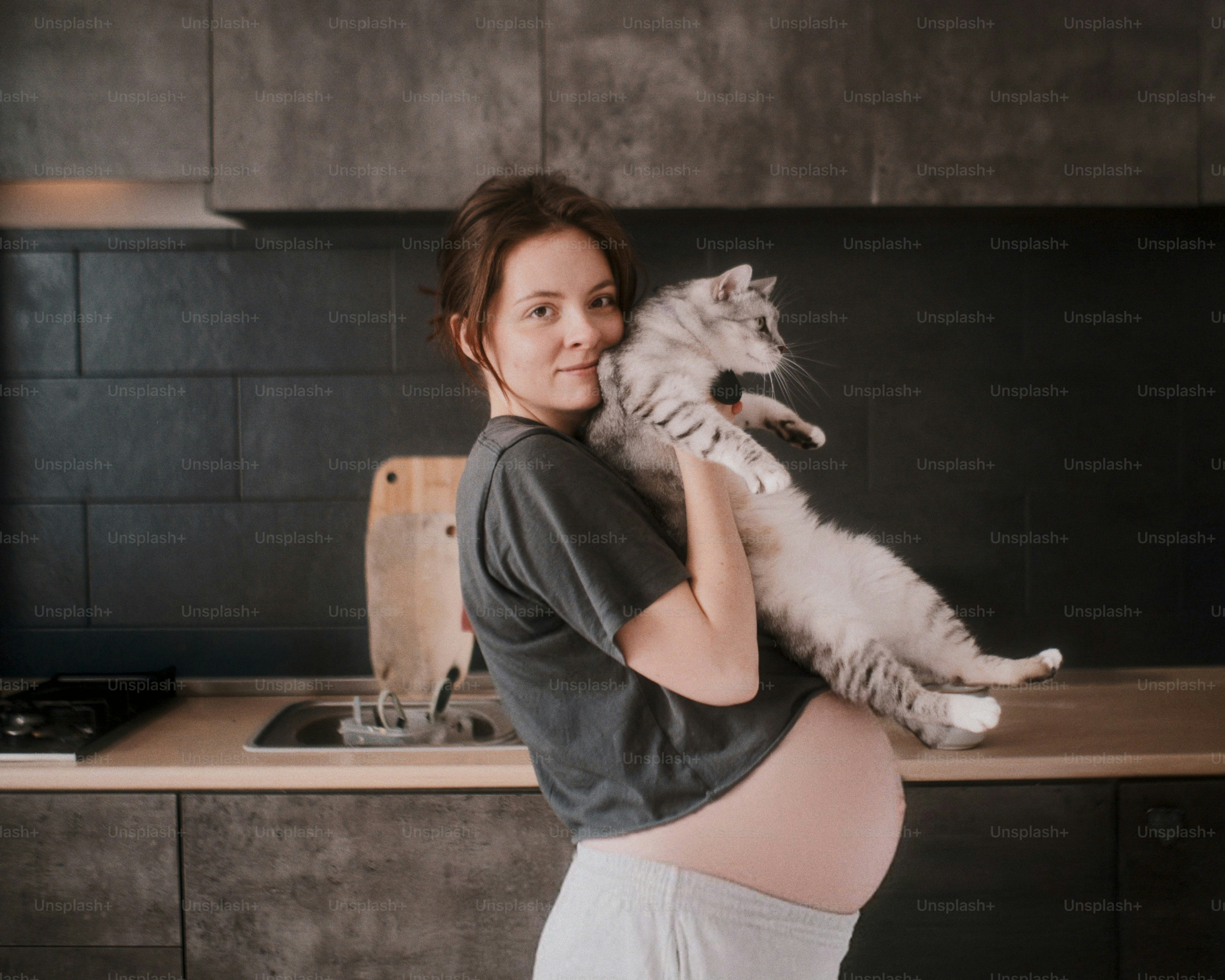 Femme enceinte tenant un chat duveteux dans une cuisine