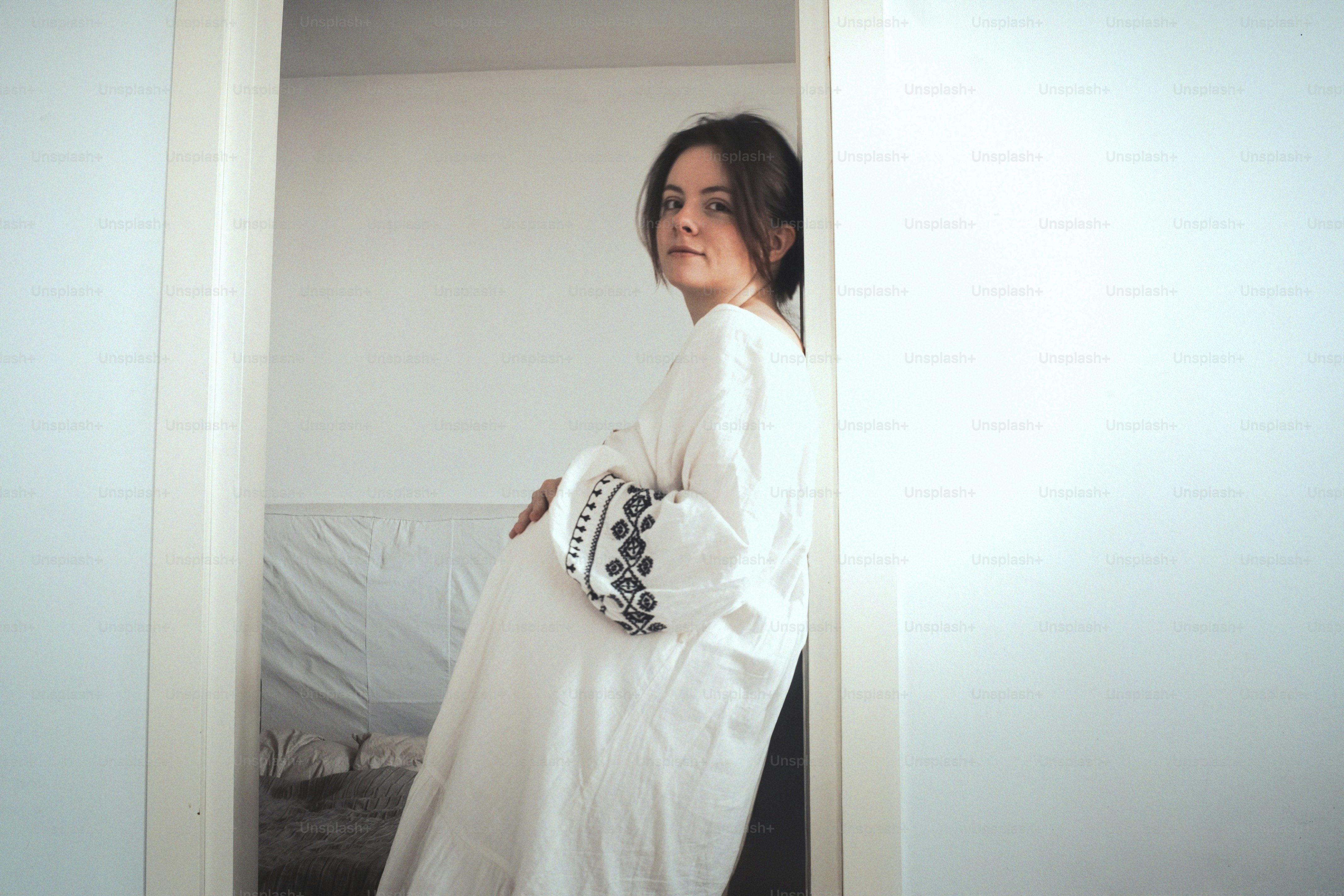 Femme enceinte en robe blanche appuyée contre le mur