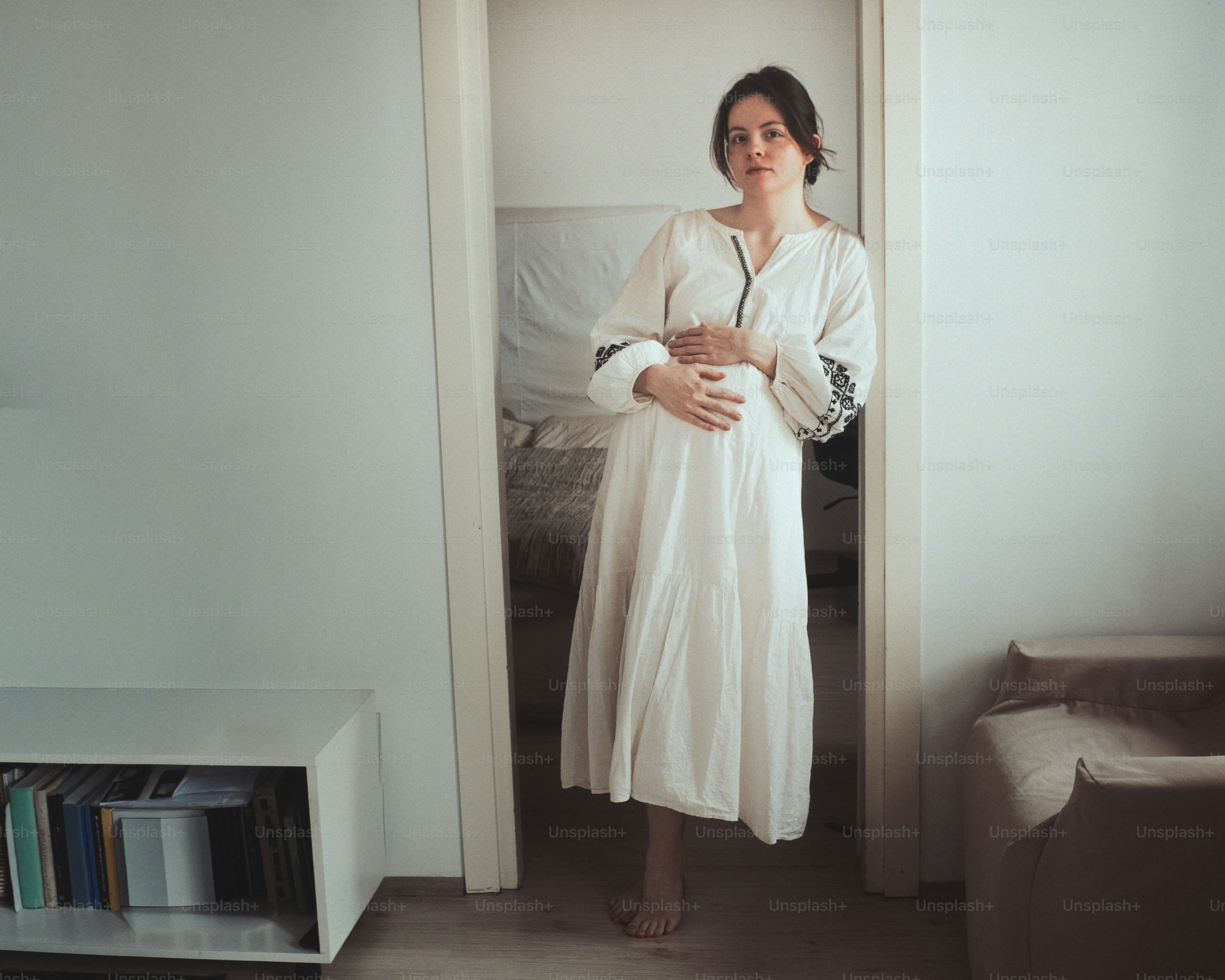 Femme enceinte en robe blanche tient son ventre.