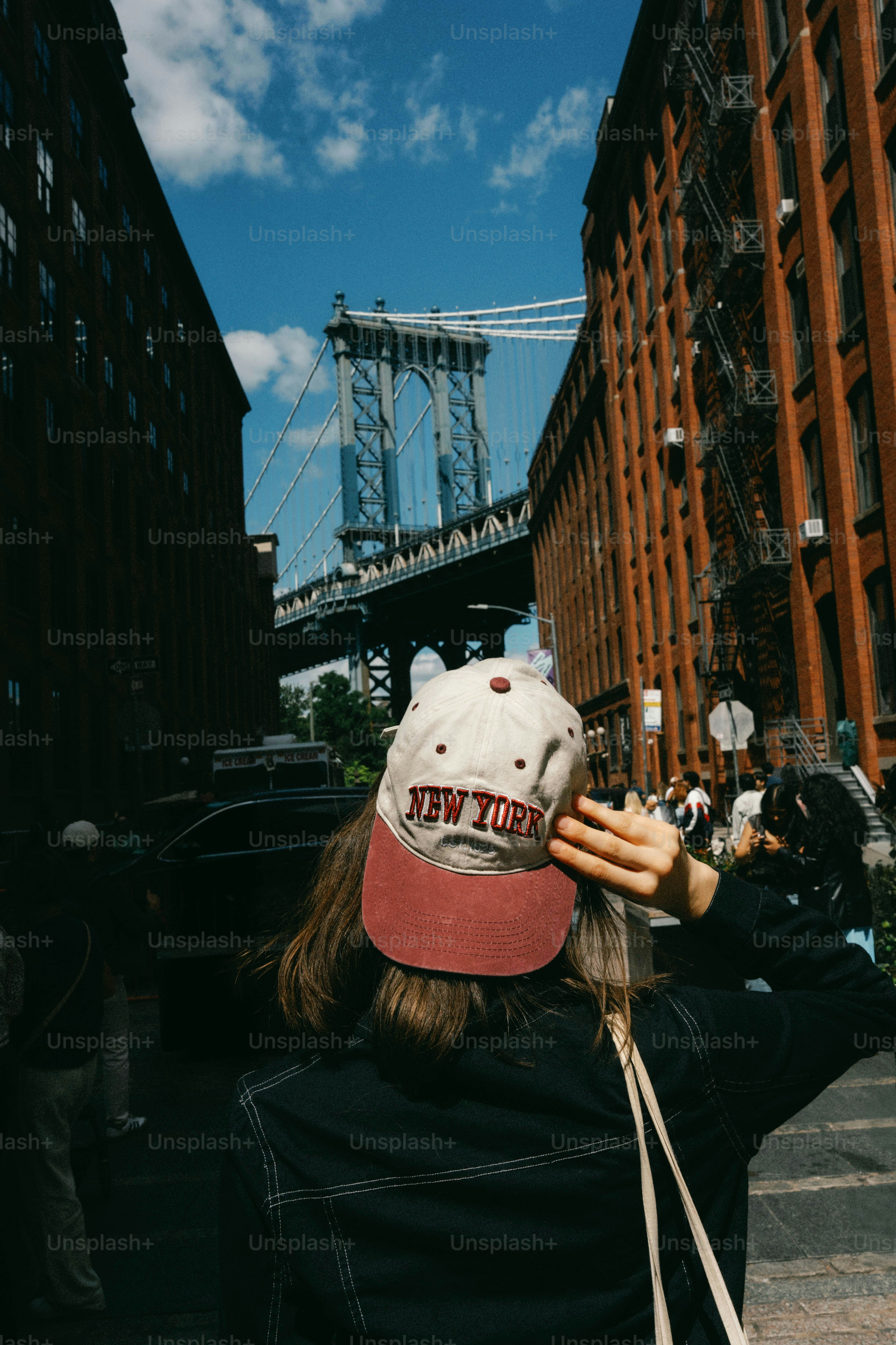 Person wearing new york hat with bridge in background.