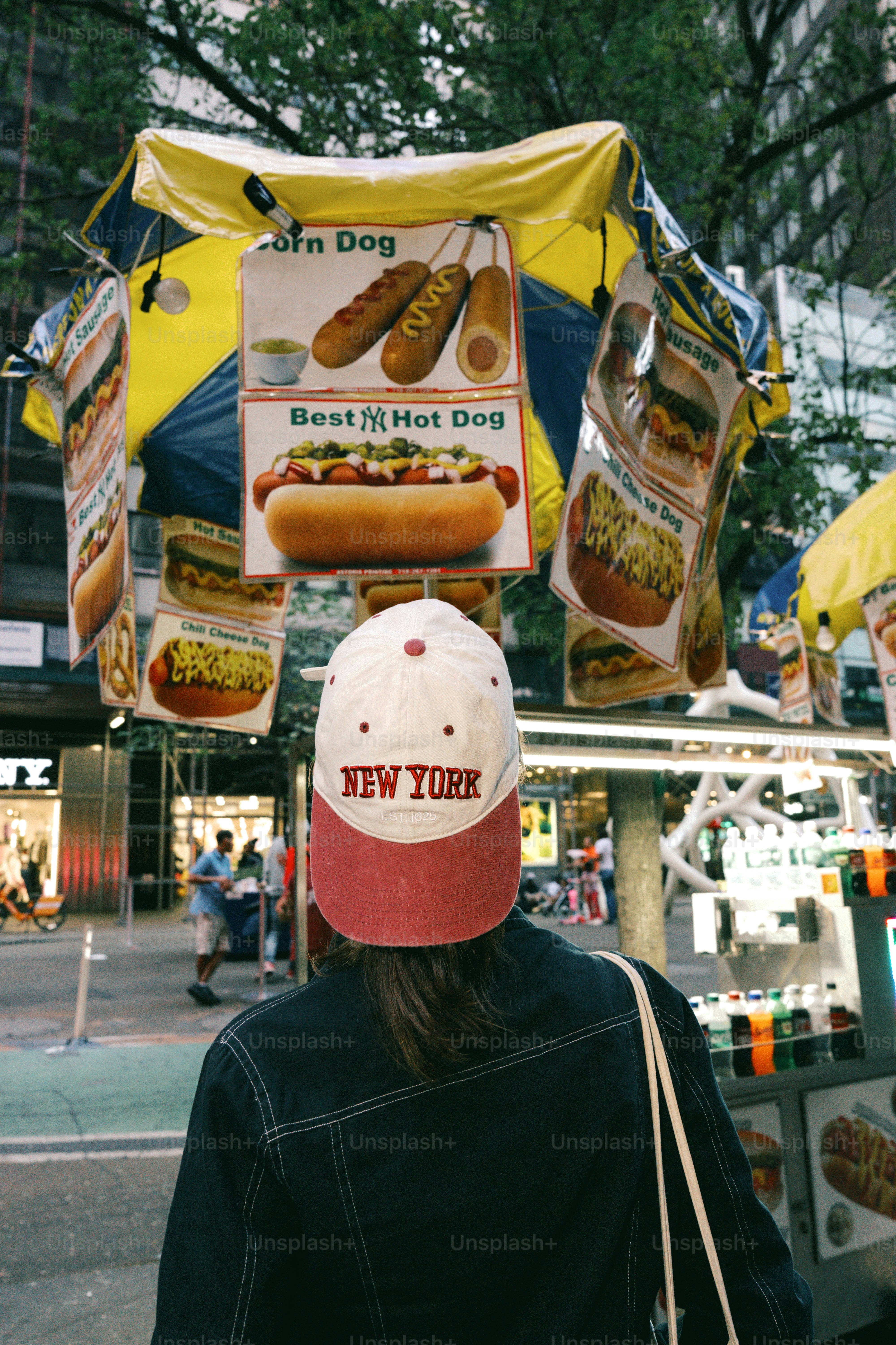 뉴욕 모자를 쓴 사람이 핫도그 가판대를 바라보고 있다