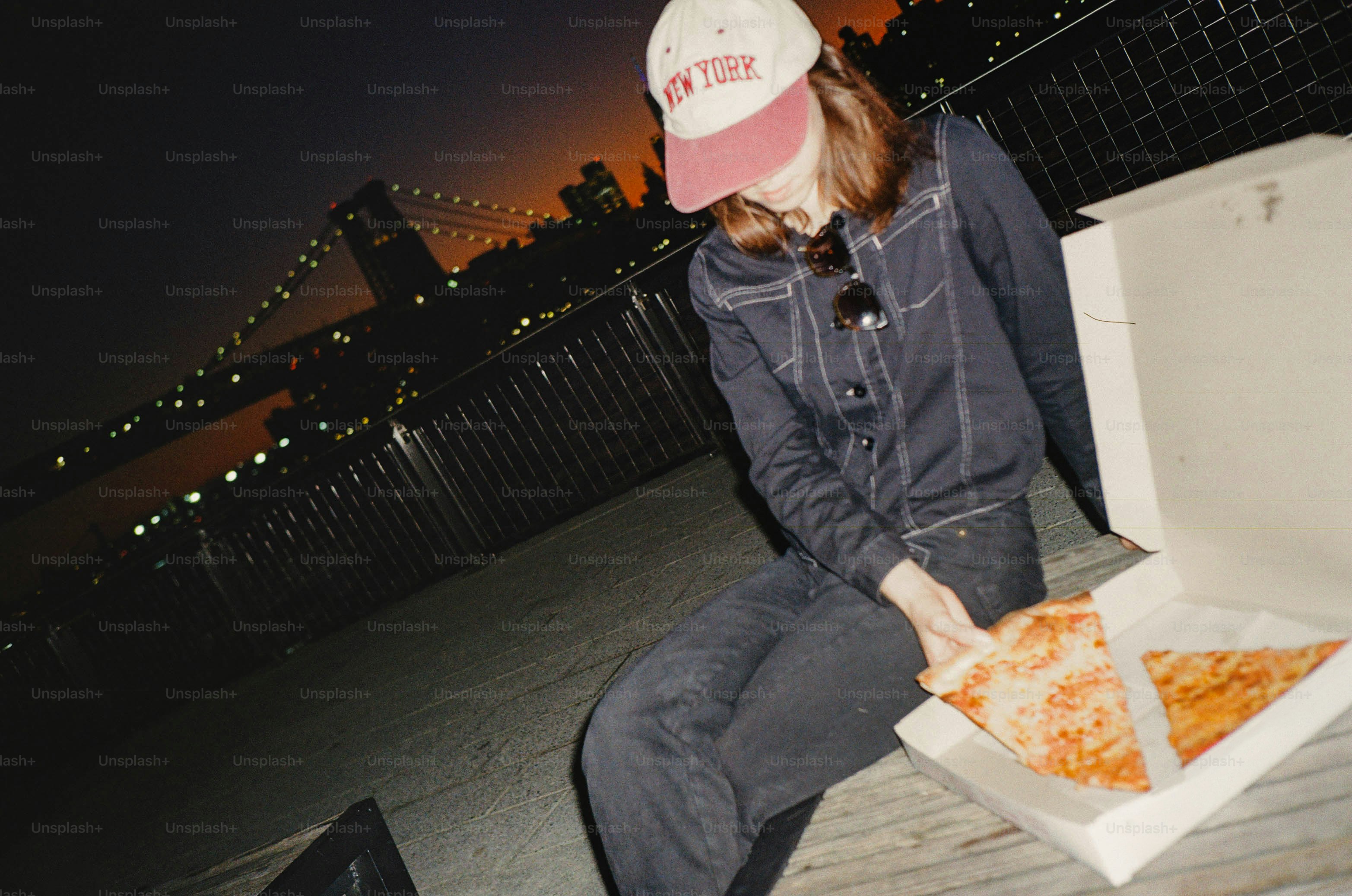 Mujer con pizza delante del puente de Brooklyn por la noche
