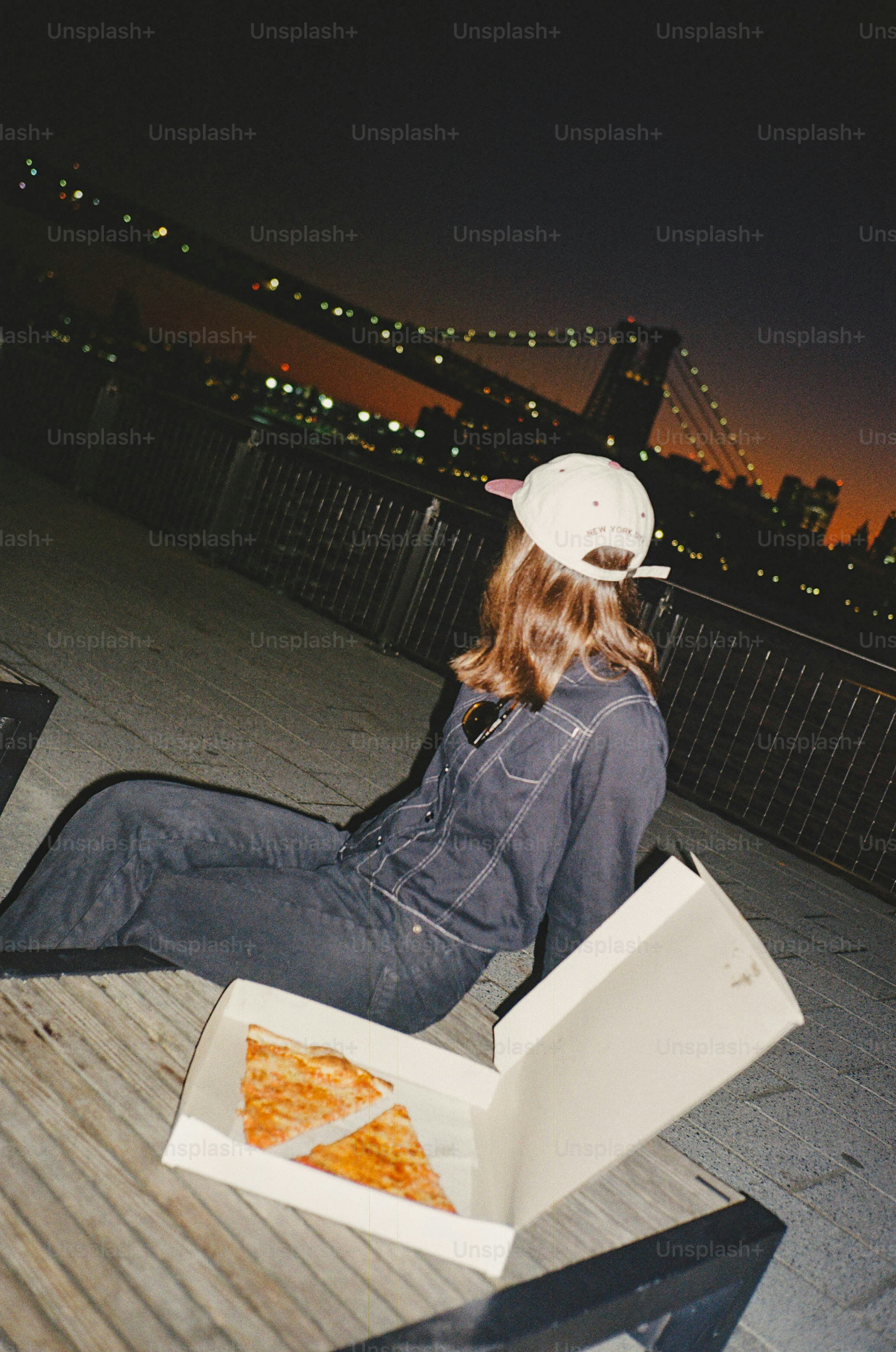 피자를 든 여자가 황혼에 도시의 불빛을 바라보고 있다