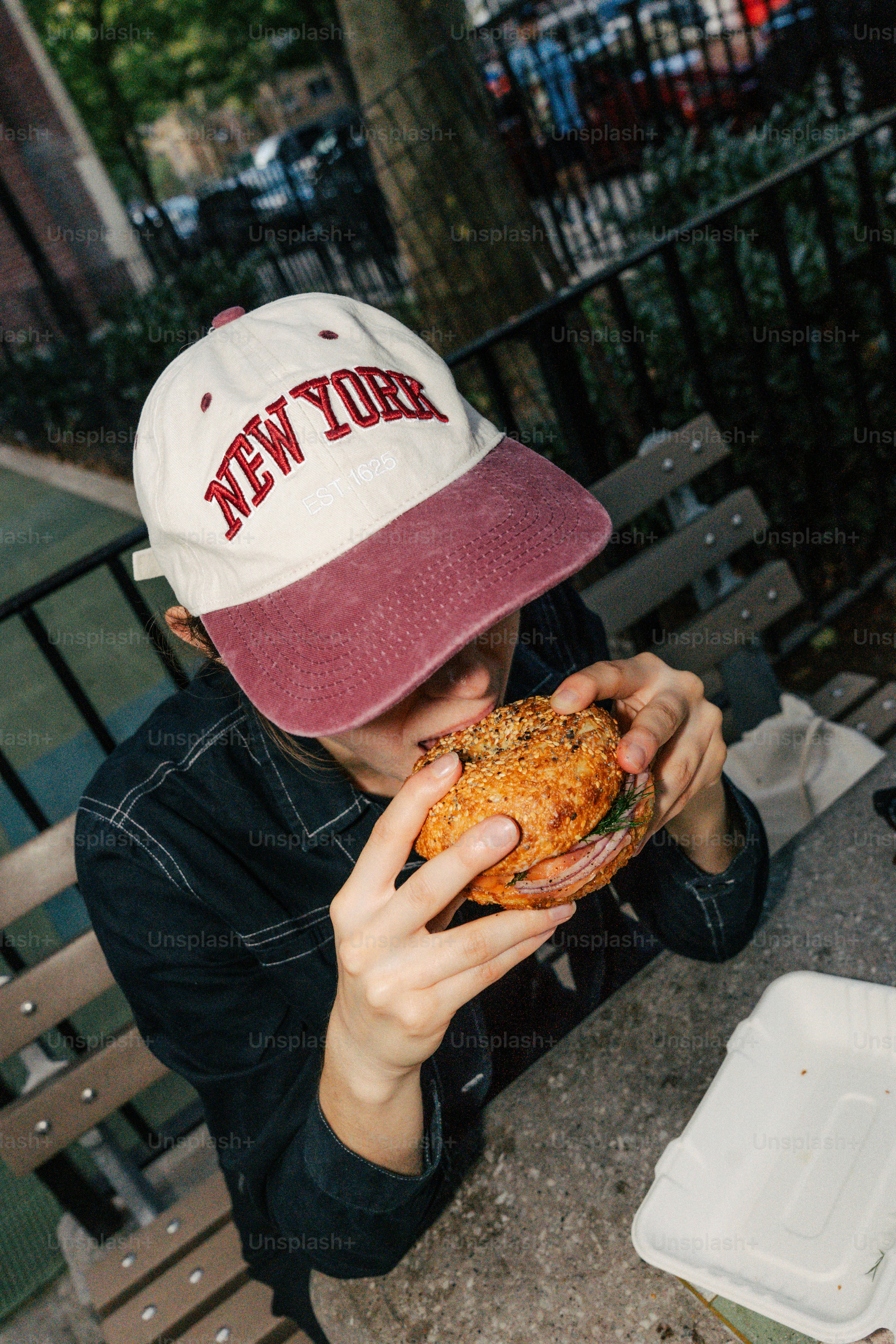 뉴욕 모자를 쓴 사람이 베이글을 먹고 있다