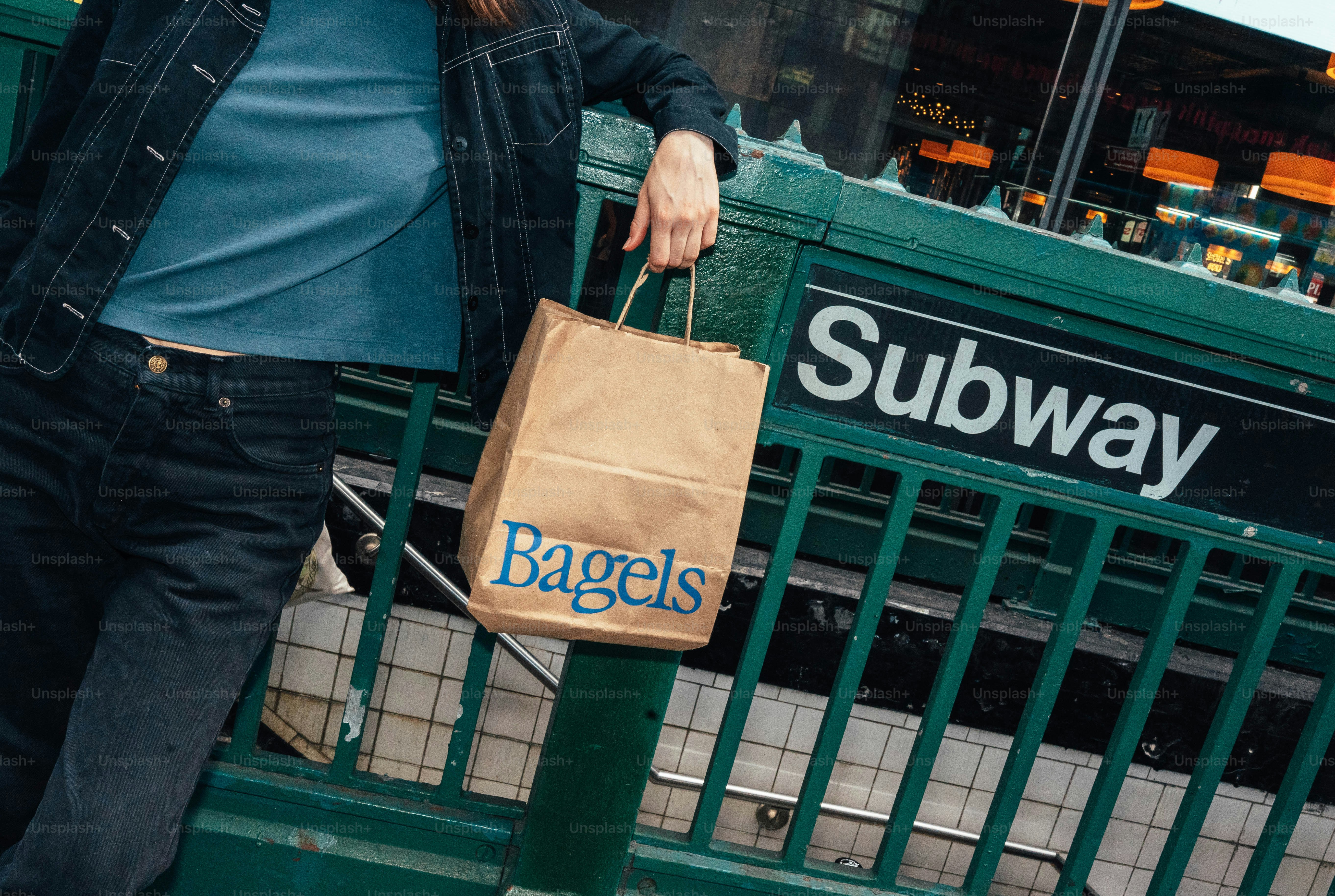 Person, die eine Bagel-Tüte in der Nähe des U-Bahn-Eingangs hält.