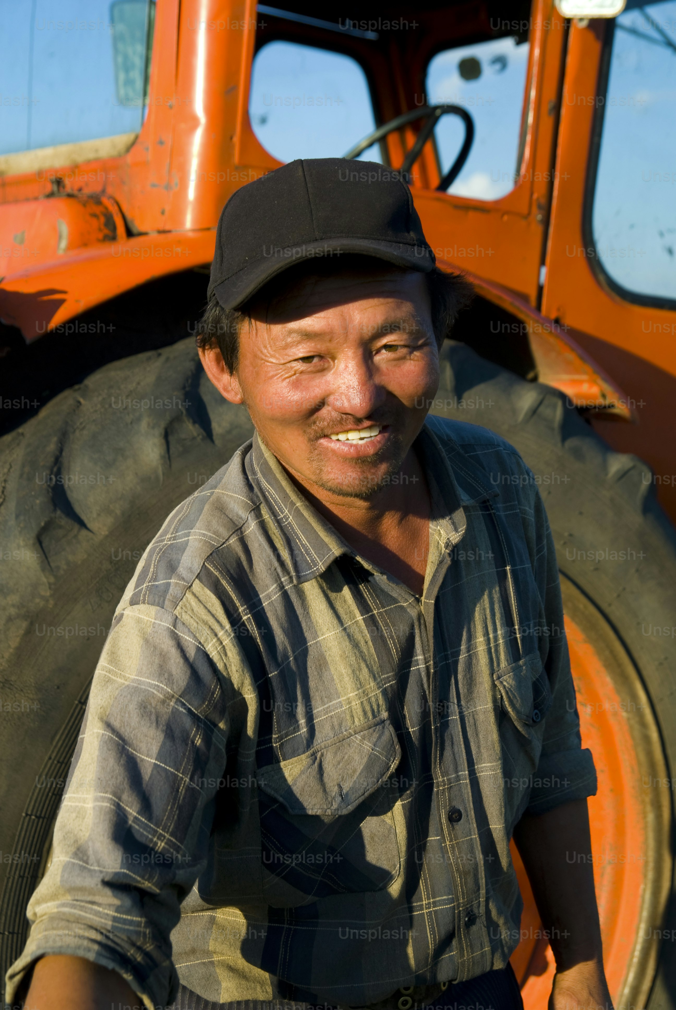 A smiling farmer stands in front of an orange tractor.