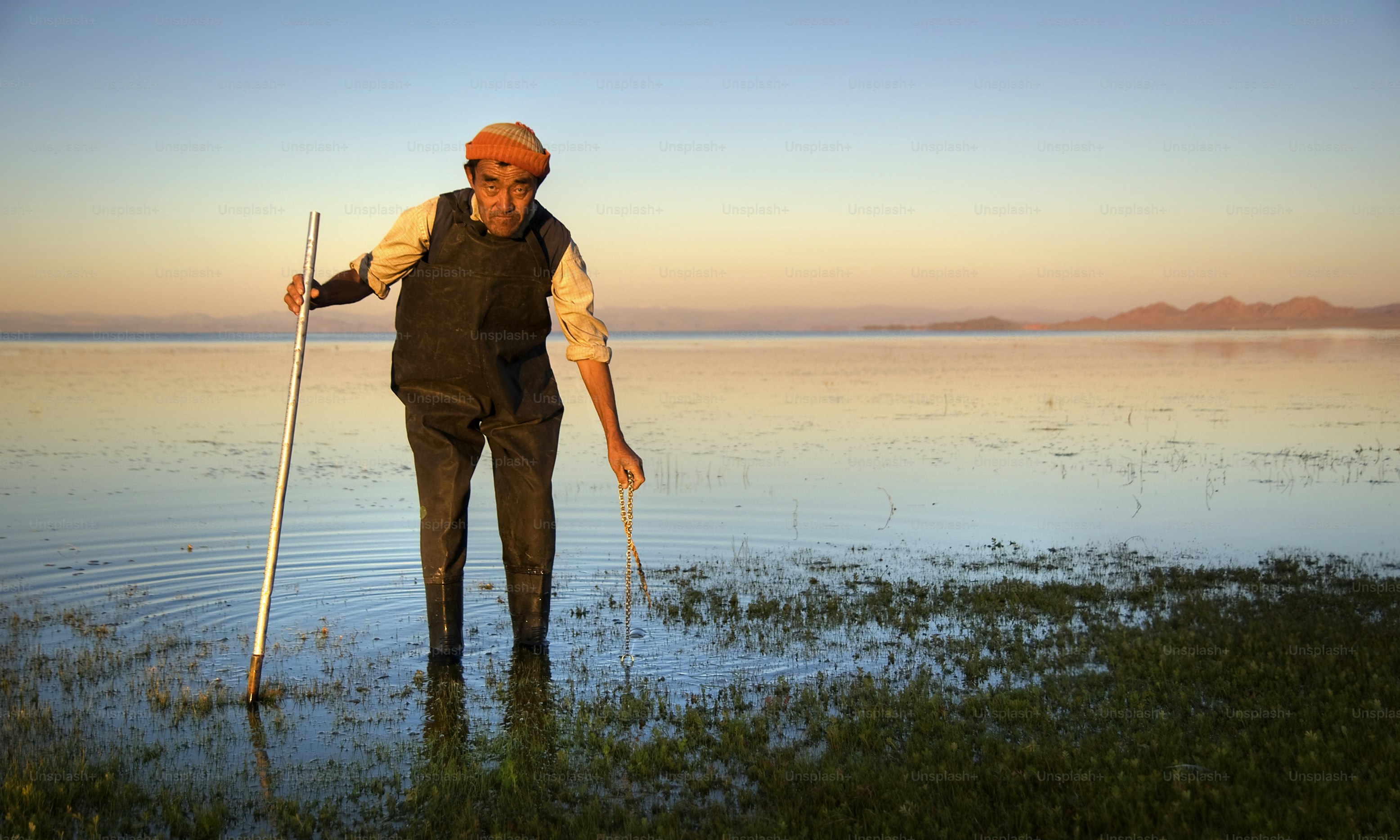 Älterer Mann mit einem Stock im seichten Wasser bei Sonnenuntergang