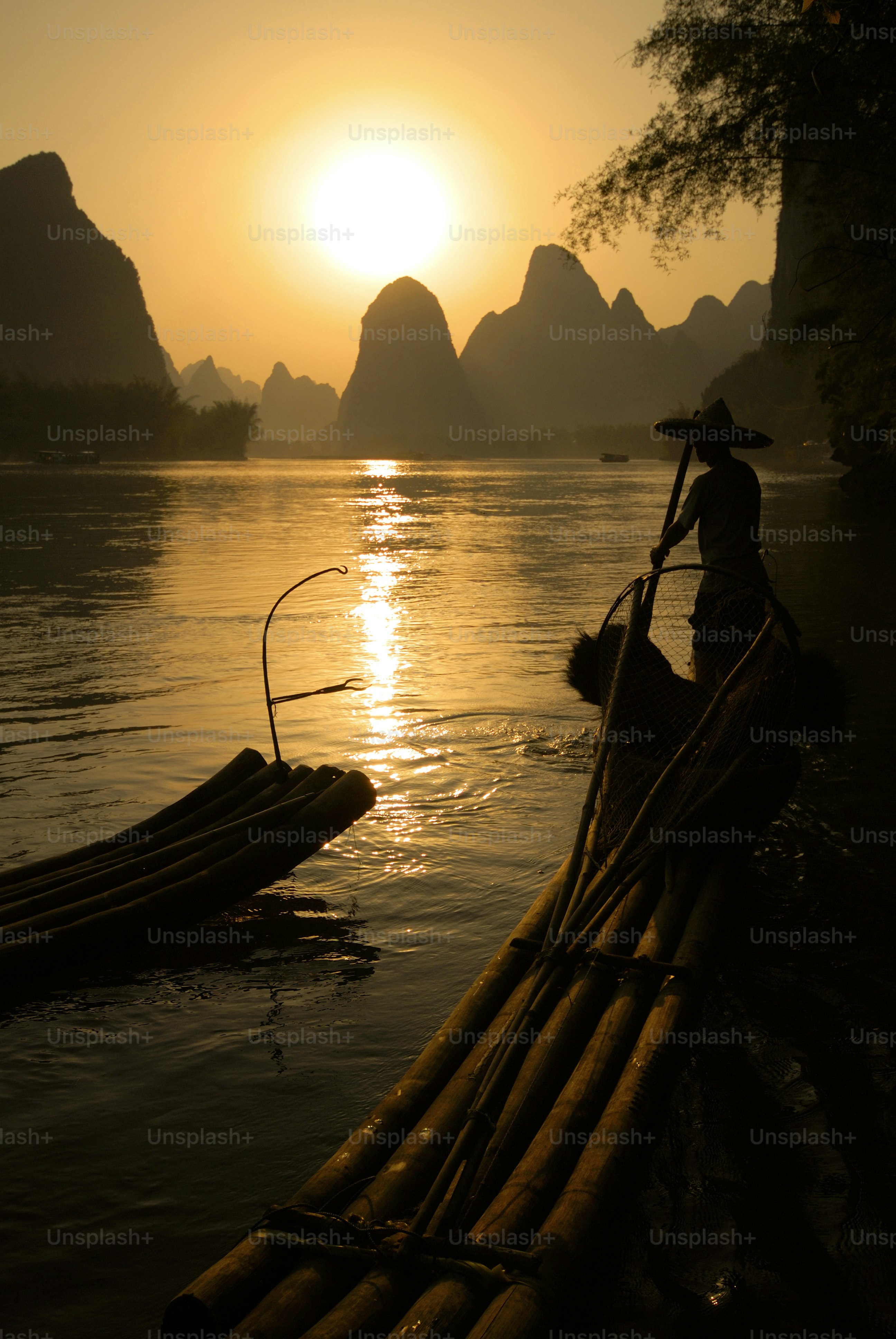 Fisherman on bamboo raft at sunset with karst mountains