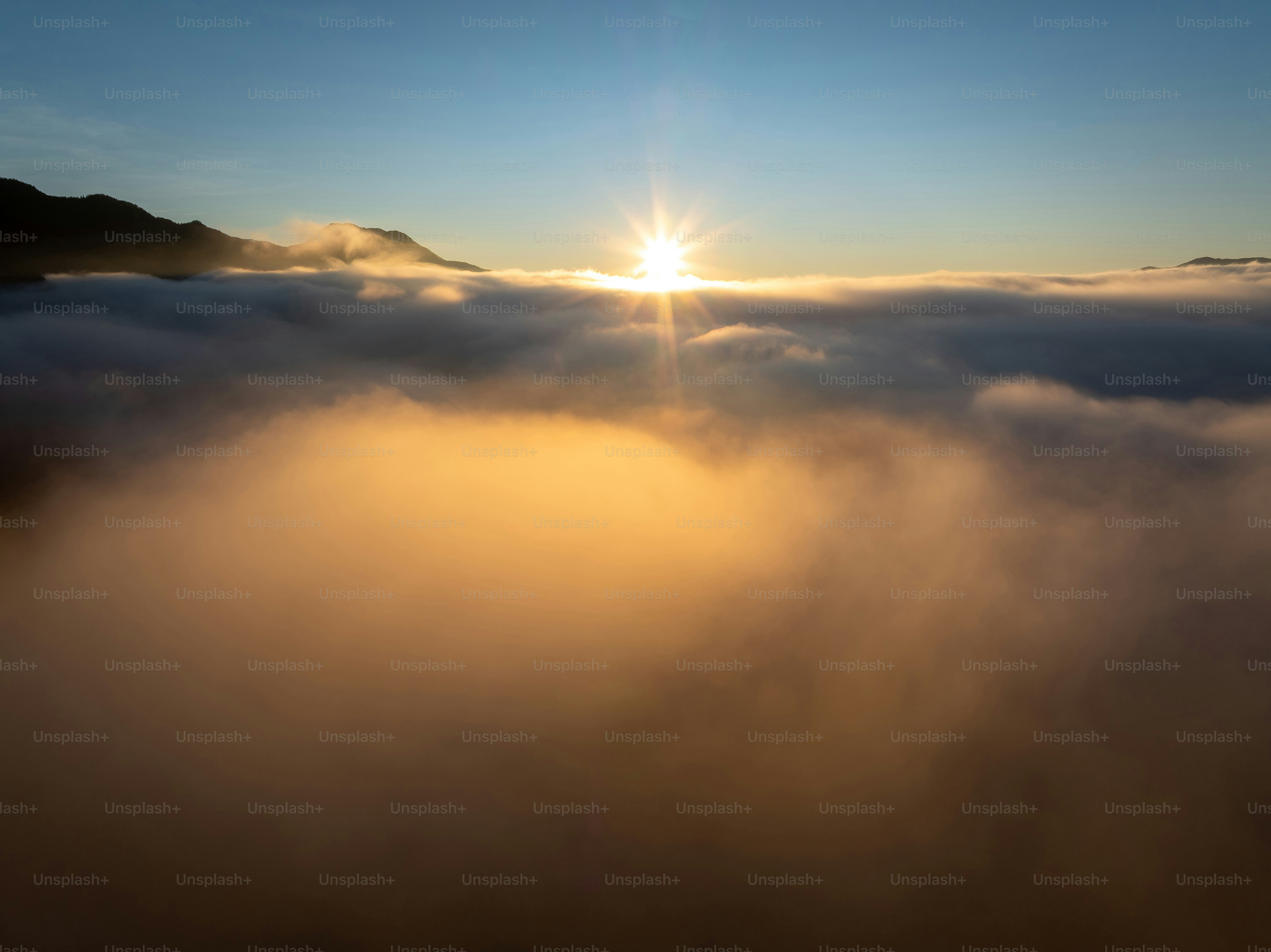 Le lever du soleil au-dessus d’une mer de nuages avec des sommets montagneux.