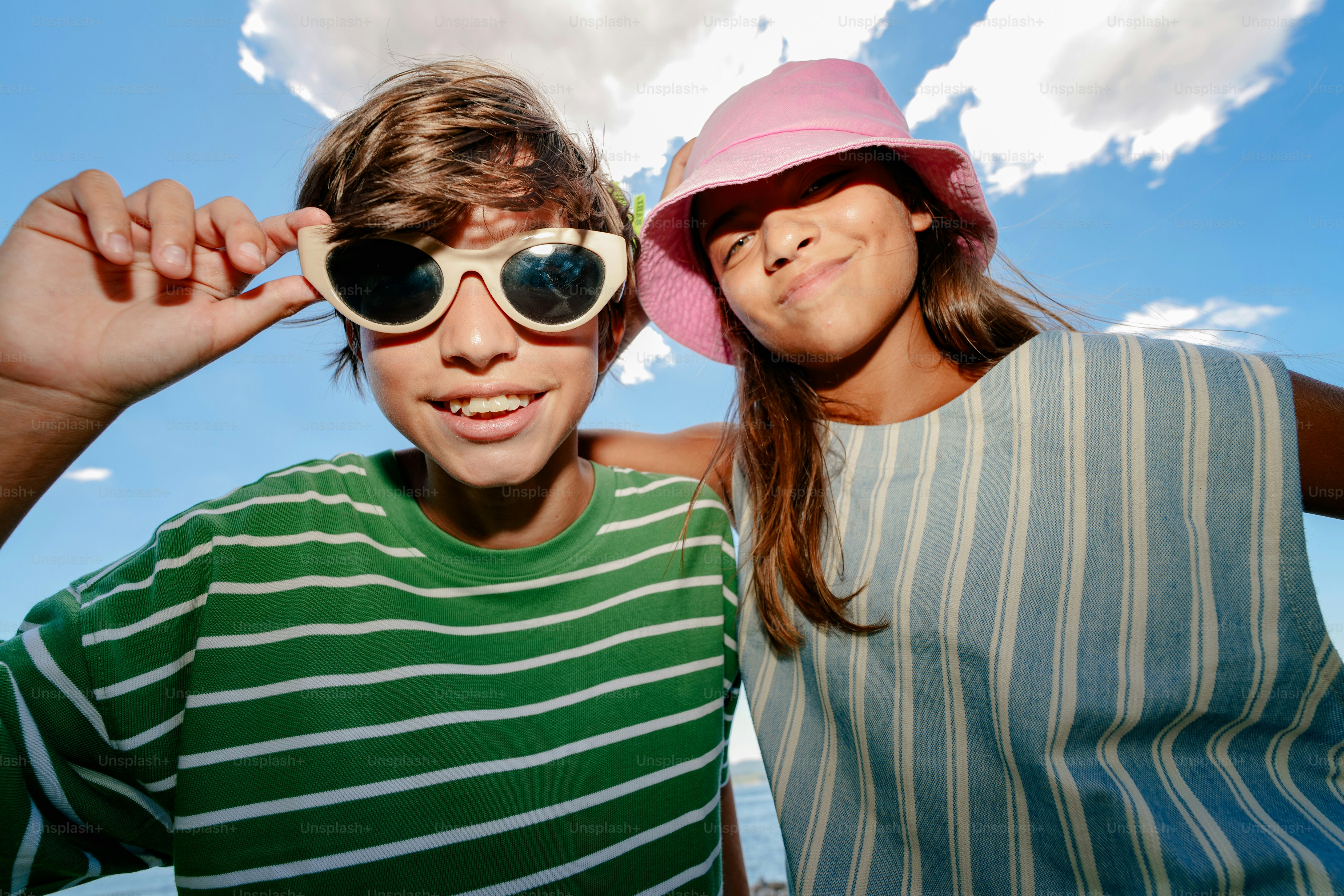 Two smiling children wearing sunglasses and a hat.