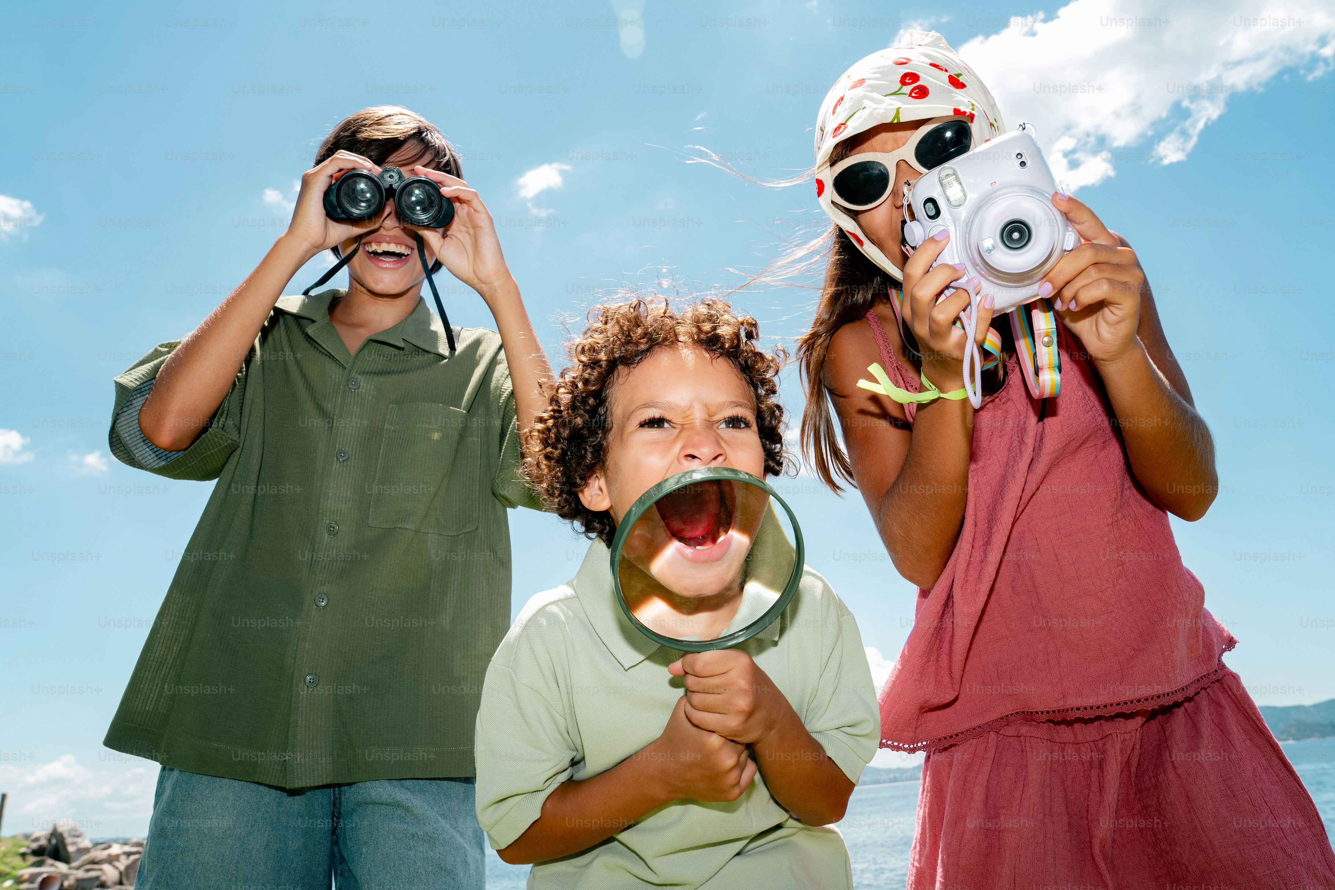 Three kids with binoculars, magnifying glass, and camera