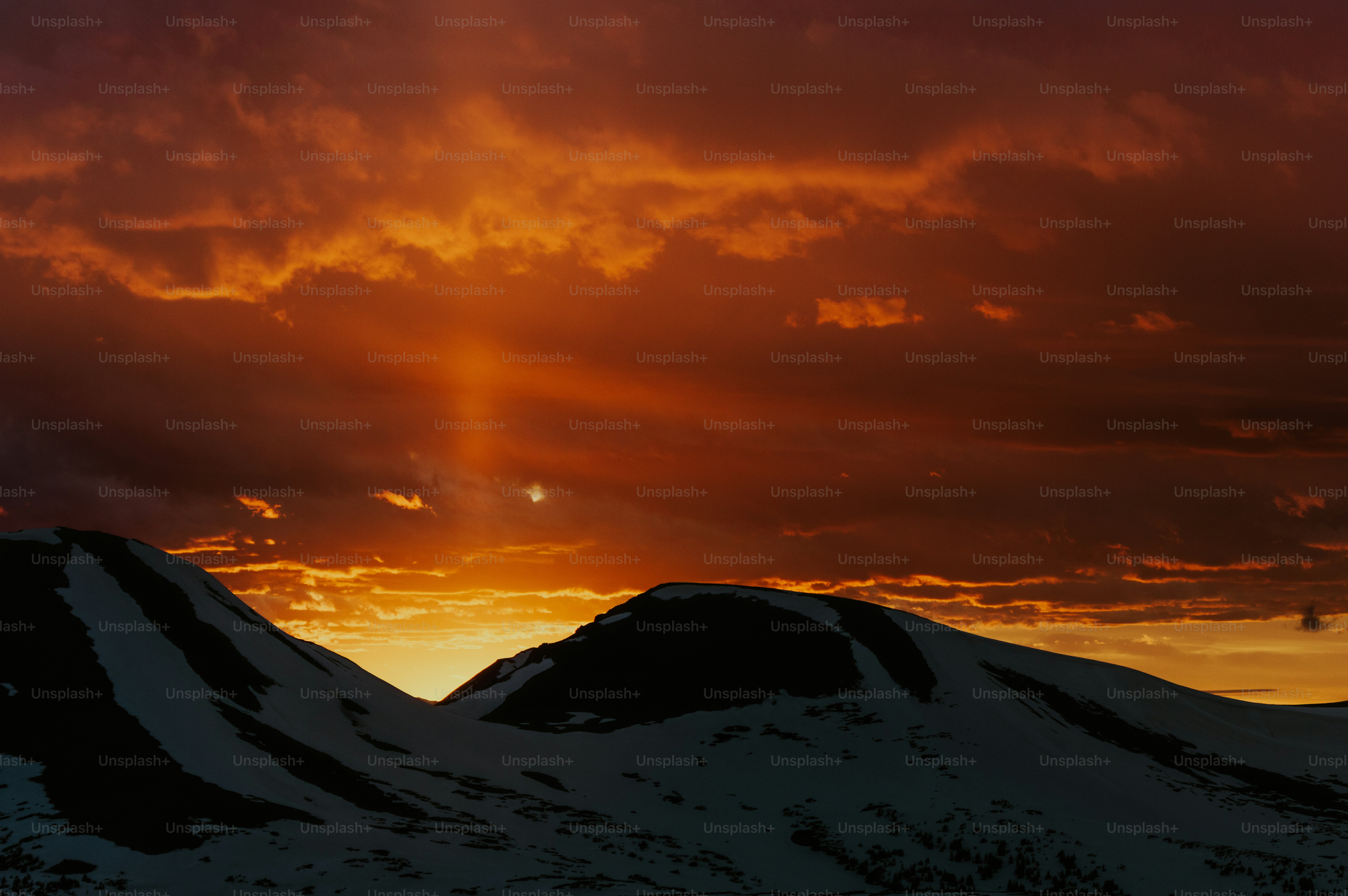 Dramatic sunset over snow-capped mountains with sunbeams