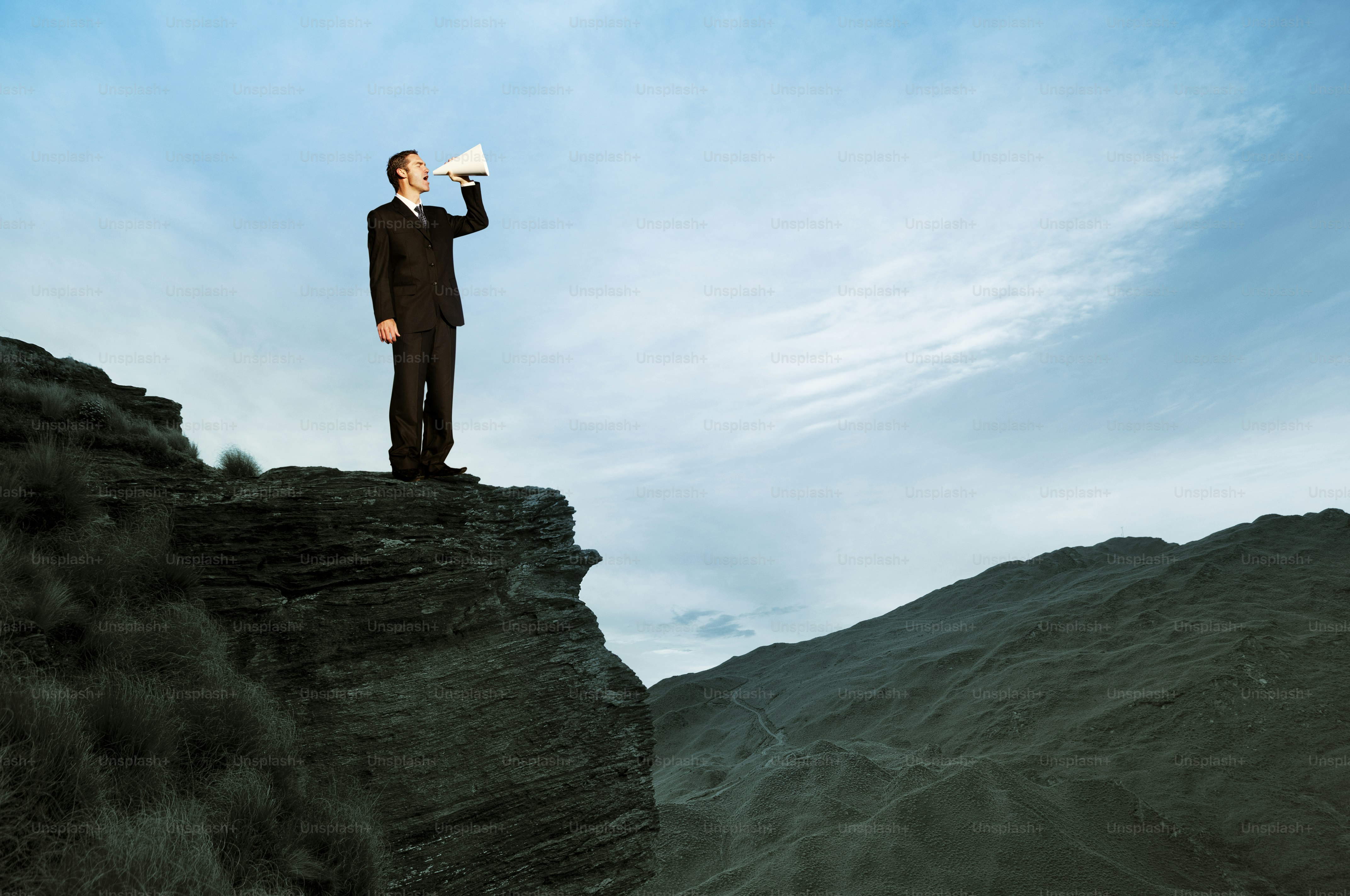 Man in suit shouts into megaphone on cliff edge
