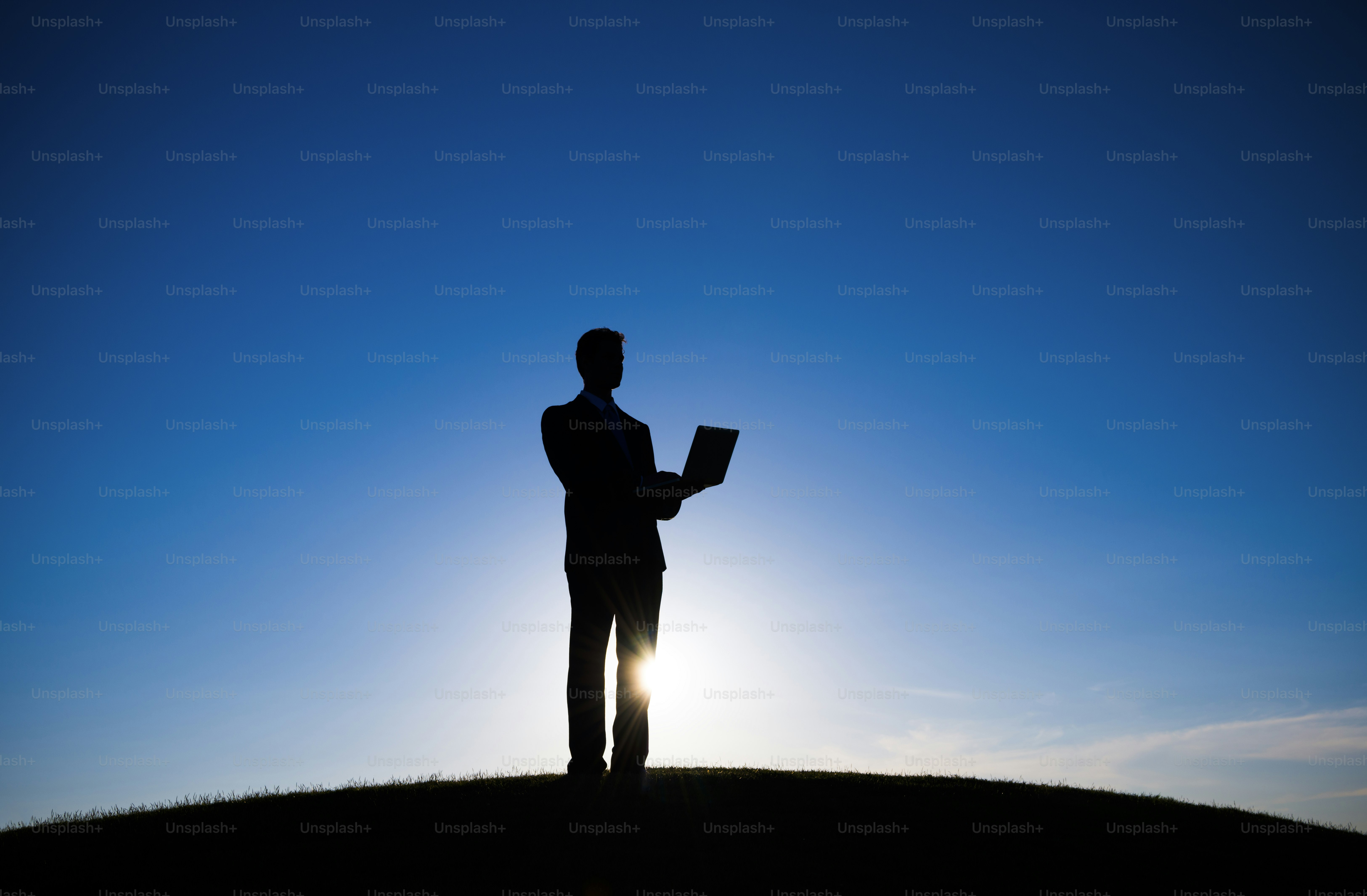 Silhouette of businessman holding laptop against bright blue sky