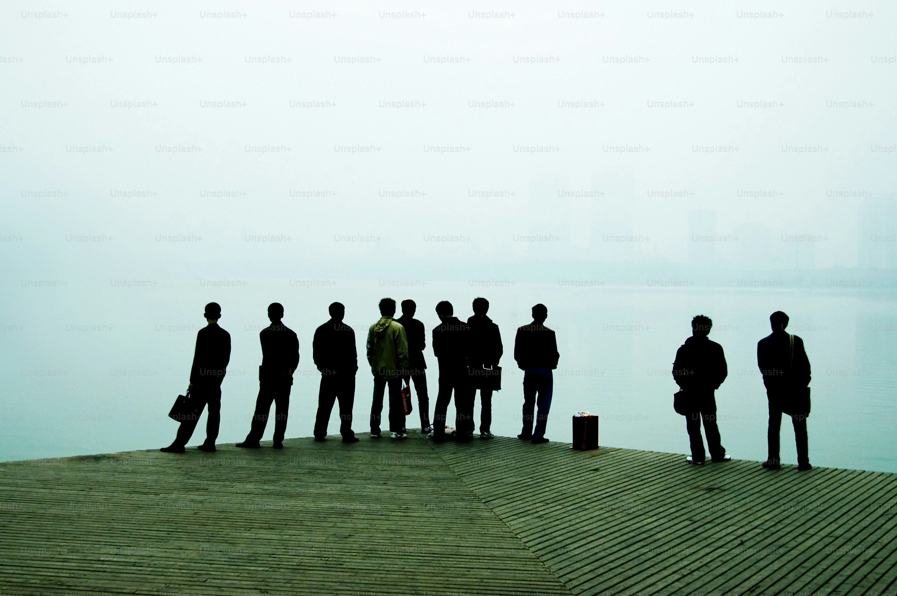 Silhouetted figures stand on a pier overlooking water
