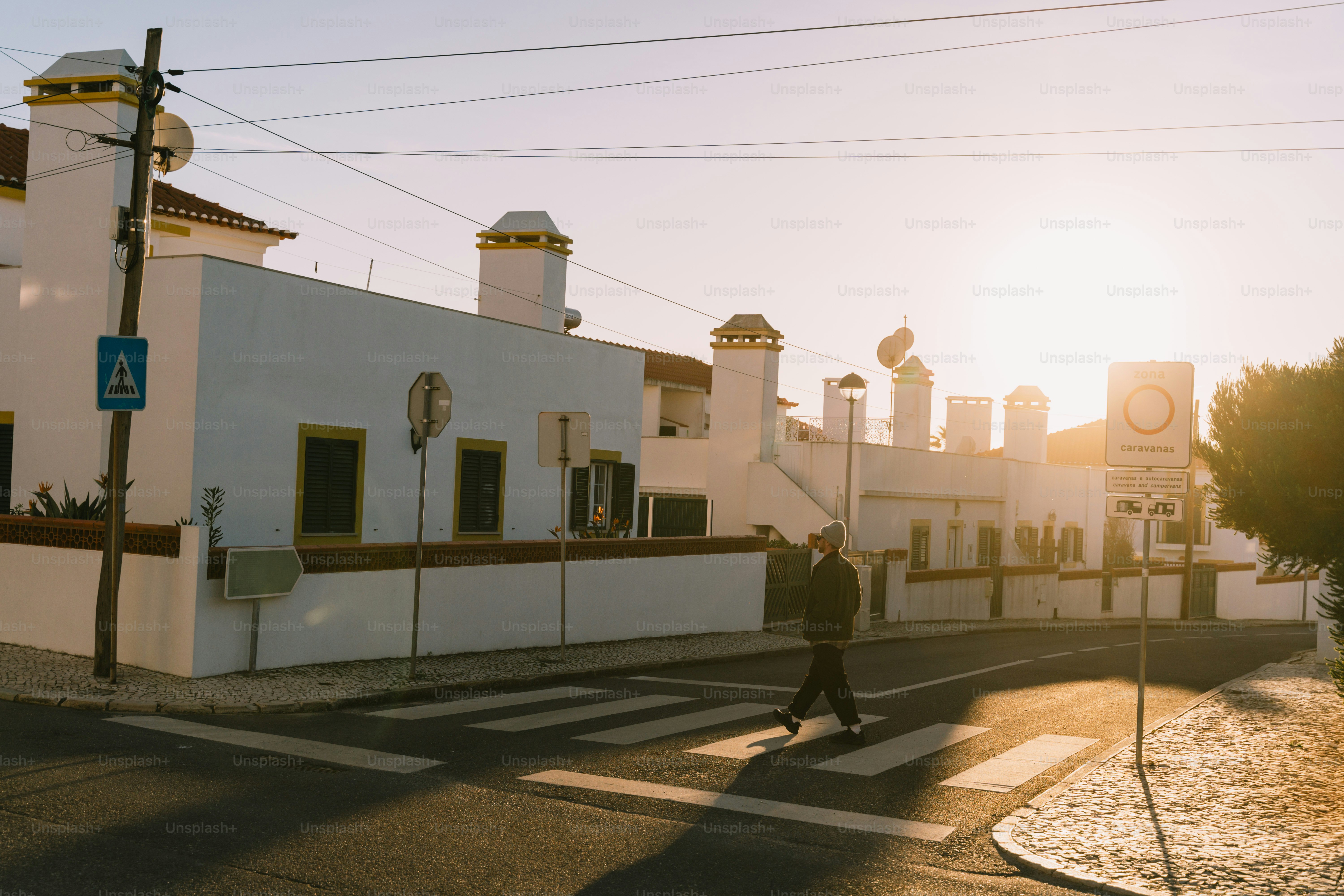 Man crossing street at sunset near white buildings.