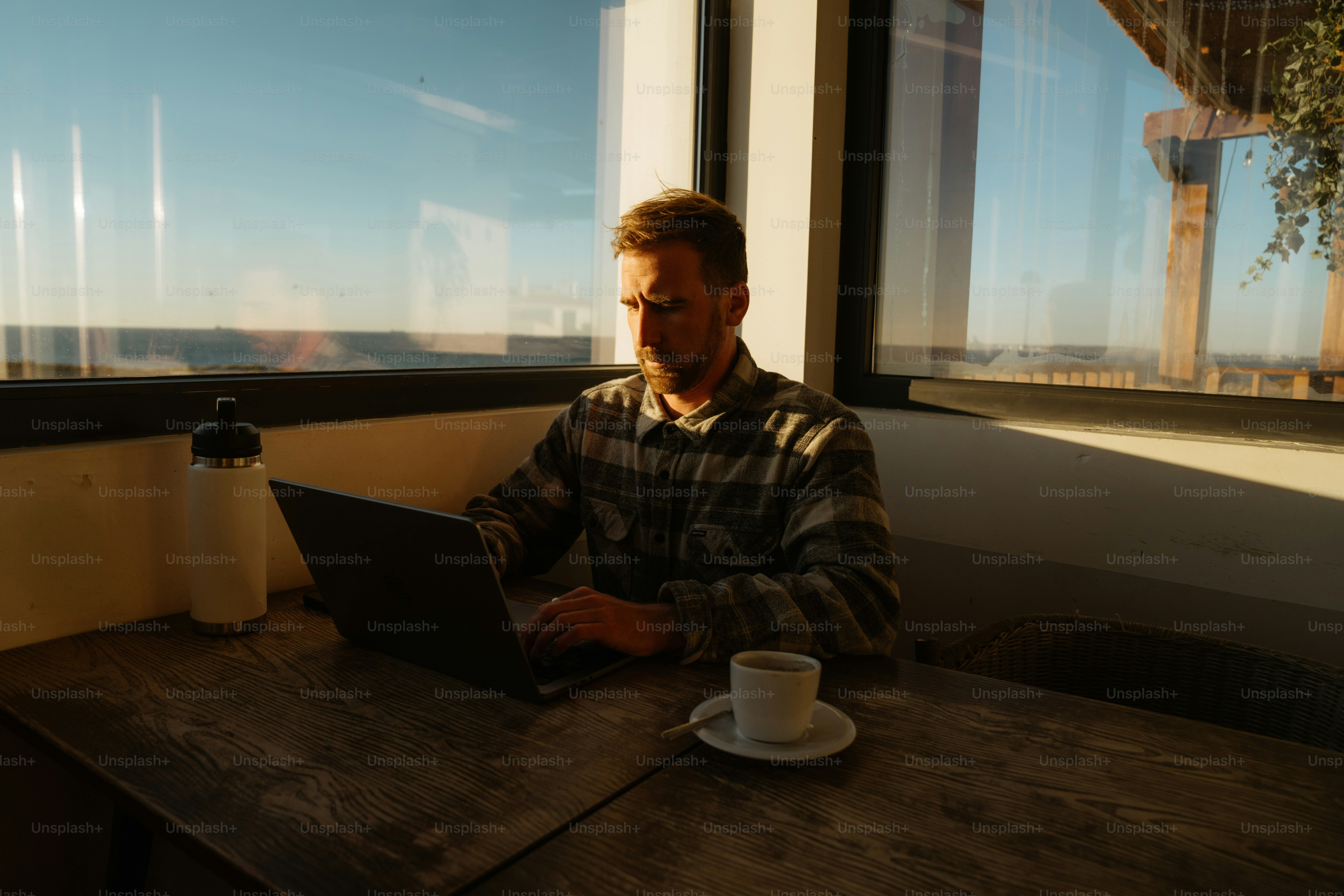 Man working on laptop with coffee by window