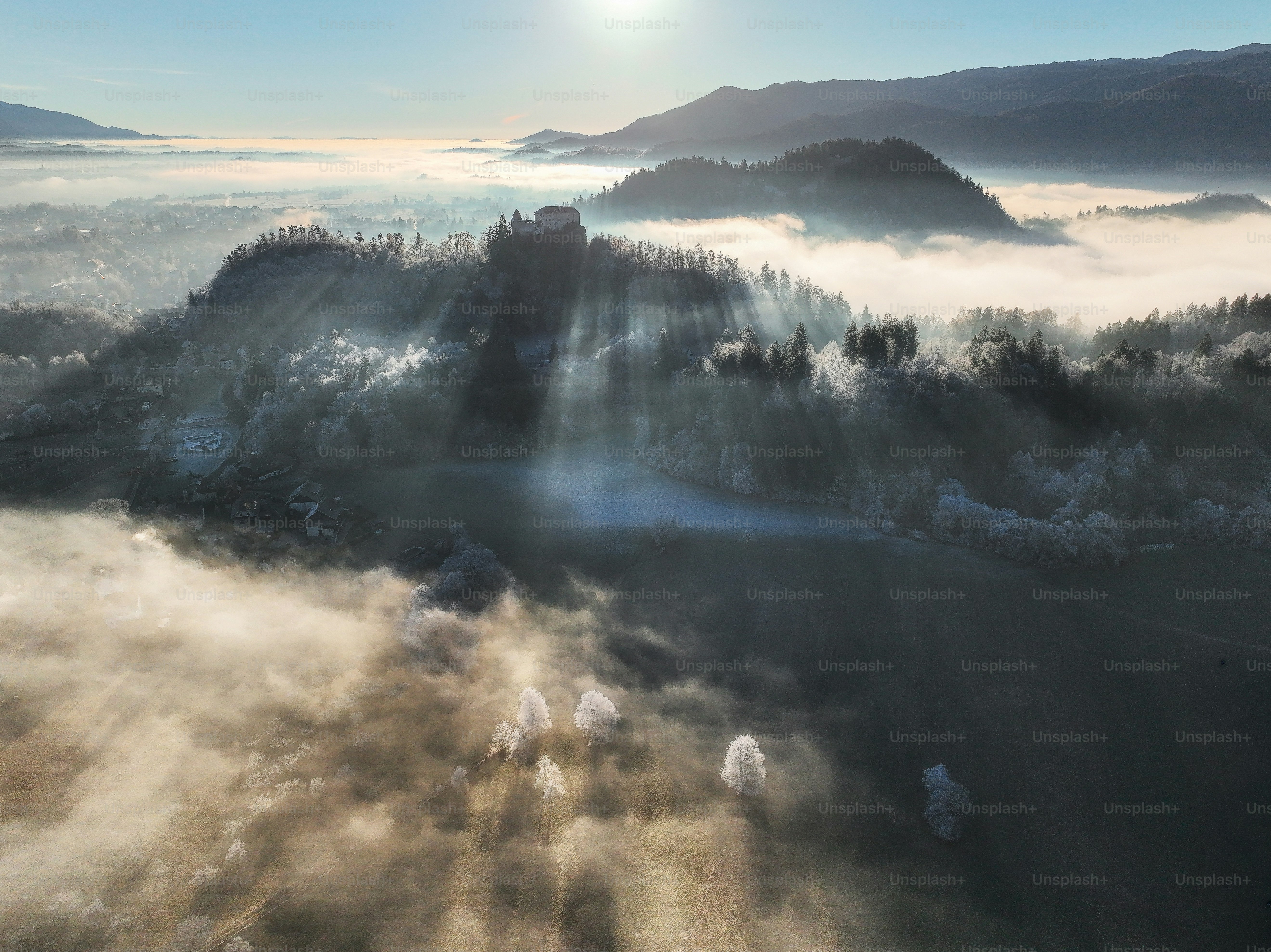 Sunlight streams through mist over a forested hill.