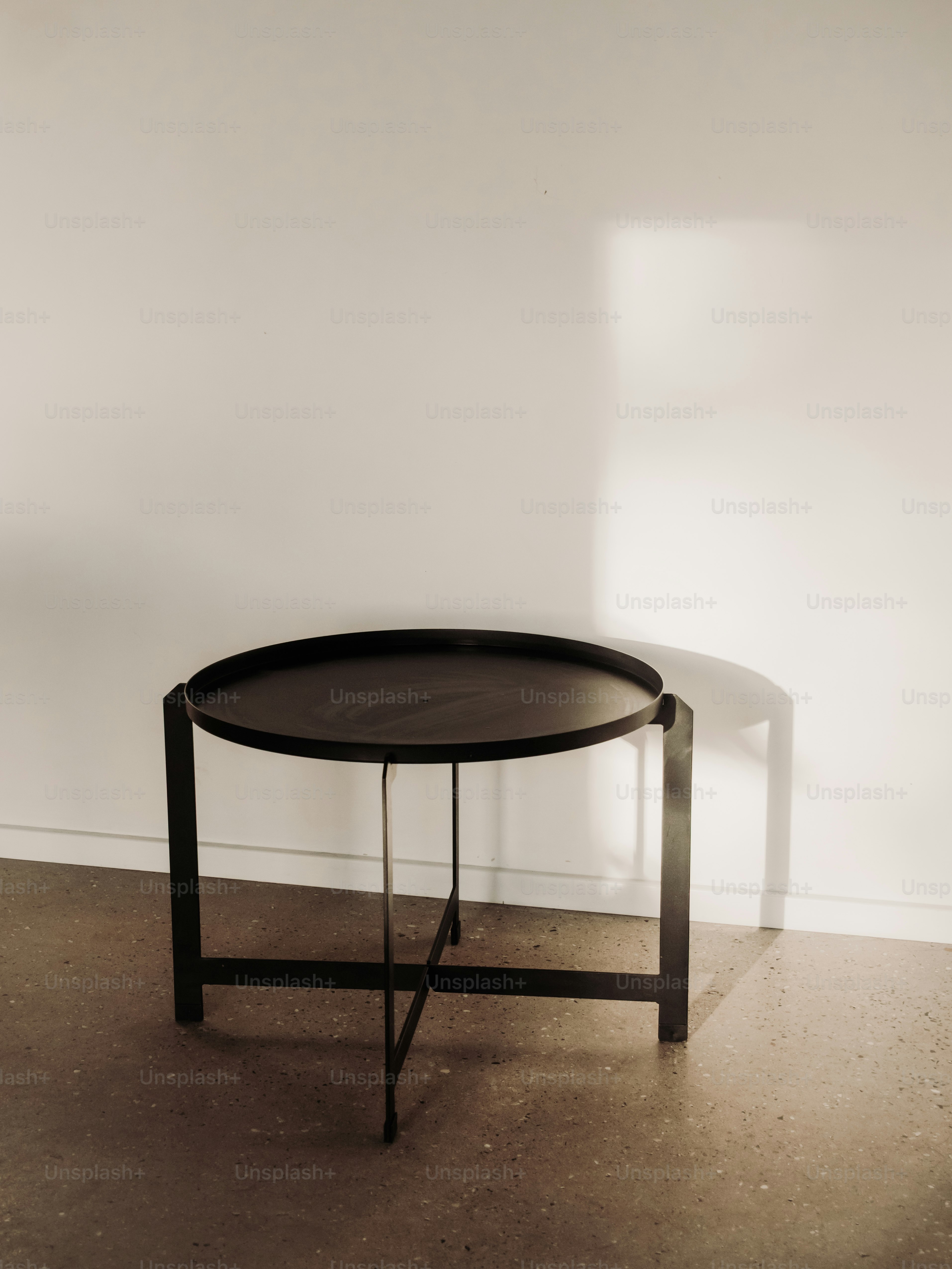 Una mesa redonda de metal negro contra una pared blanca.