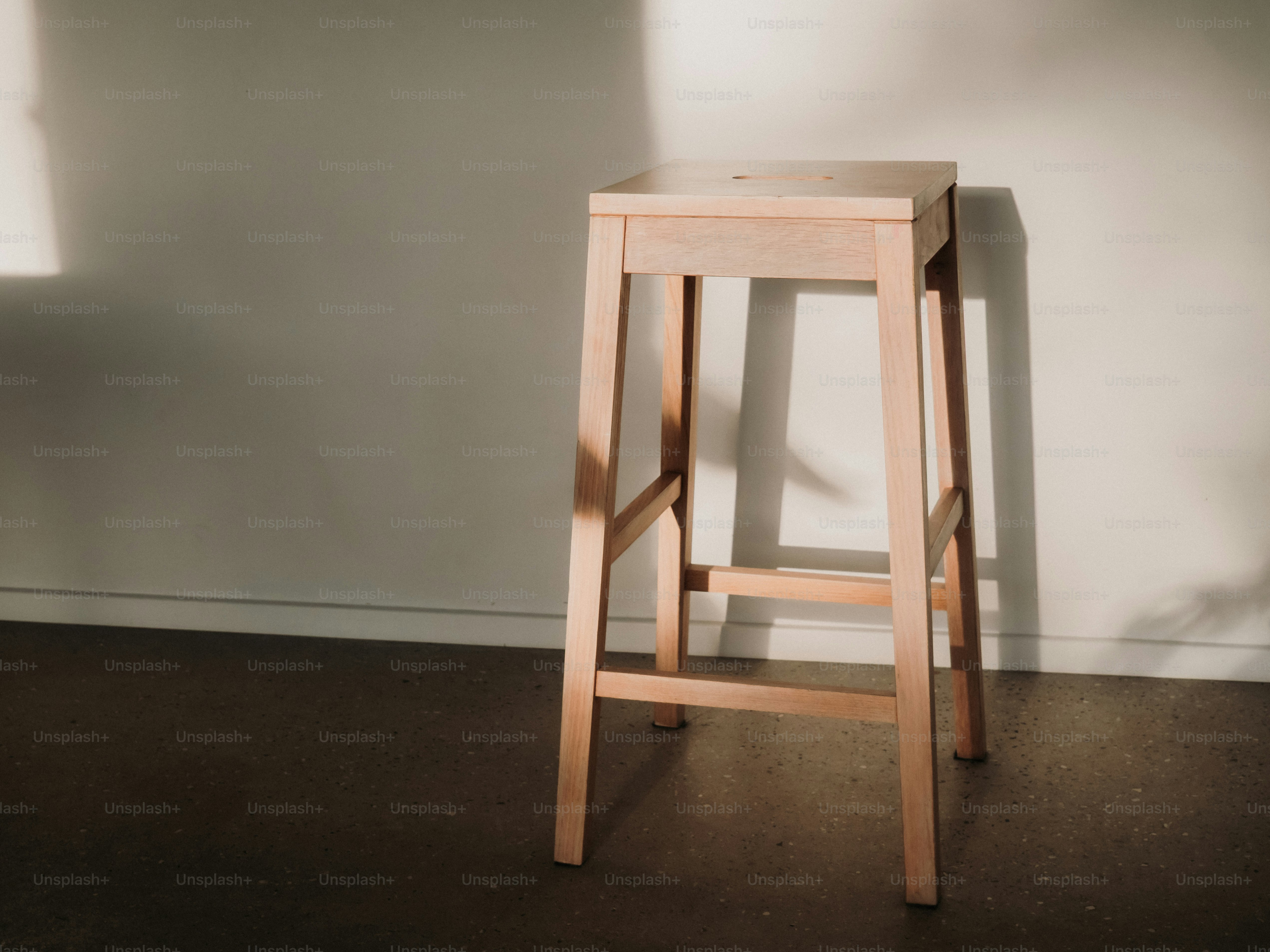 Holzbarhocker in warmem Sonnenlicht nahe der Wand.