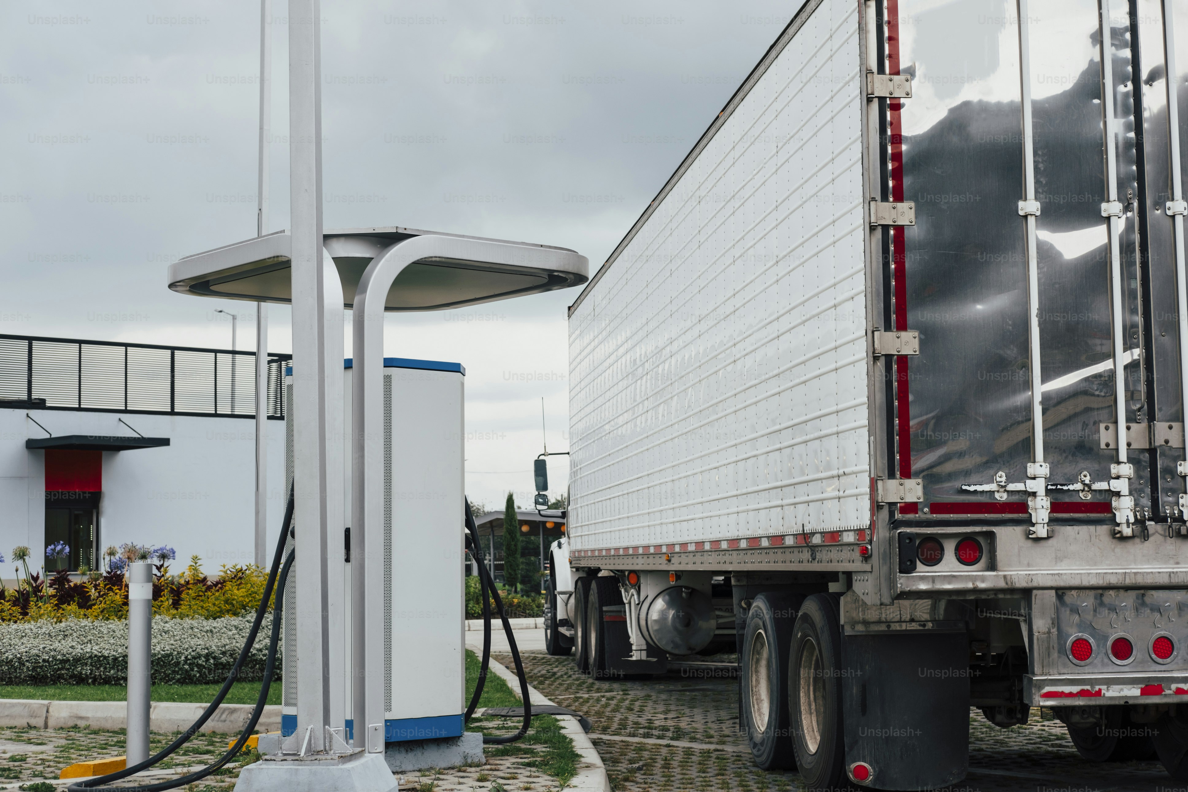 하얀 대형 트럭이 충전 스테이션에 주차되어 있다.