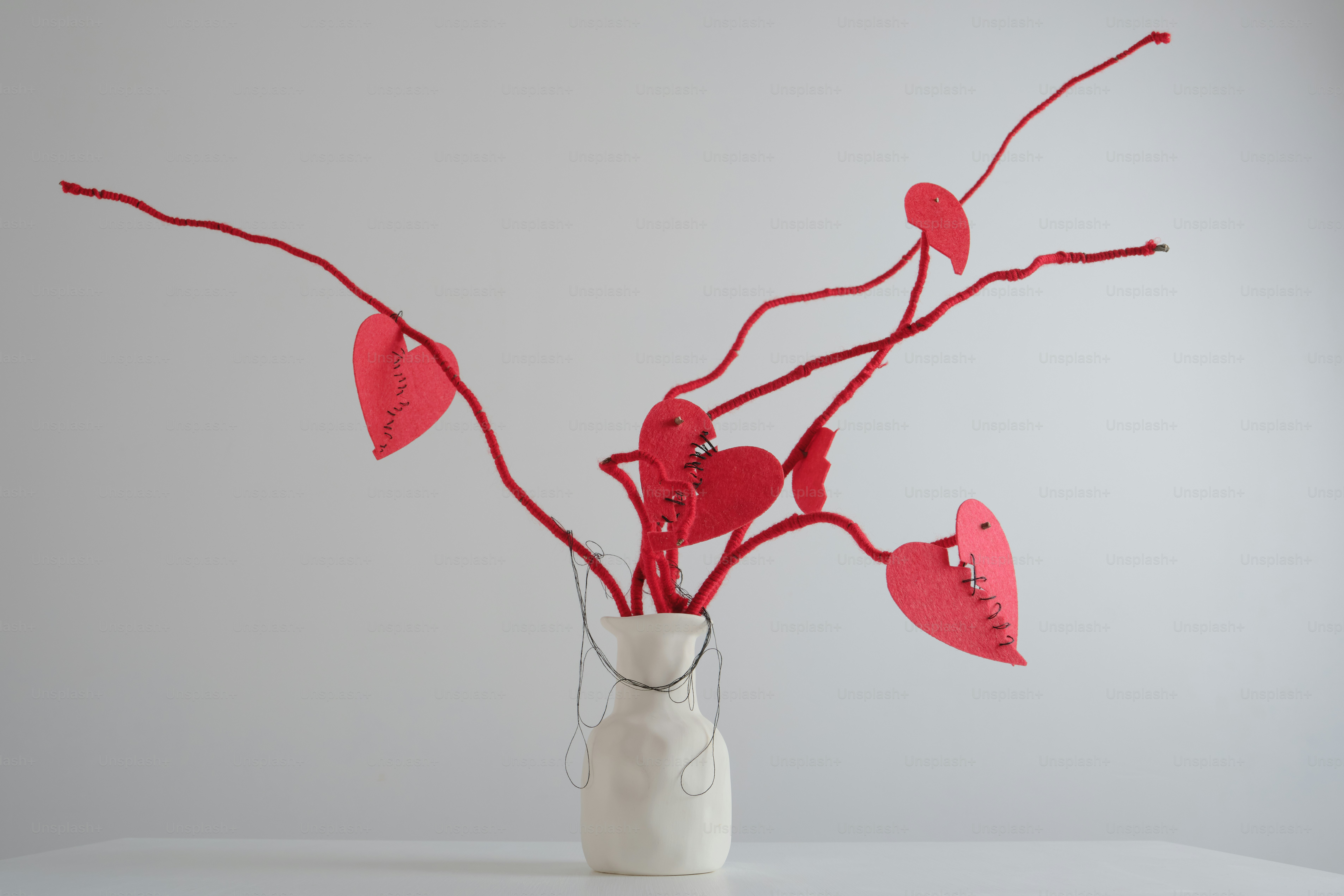 Ornamenti a cuore rosso sui rami in un vaso bianco.