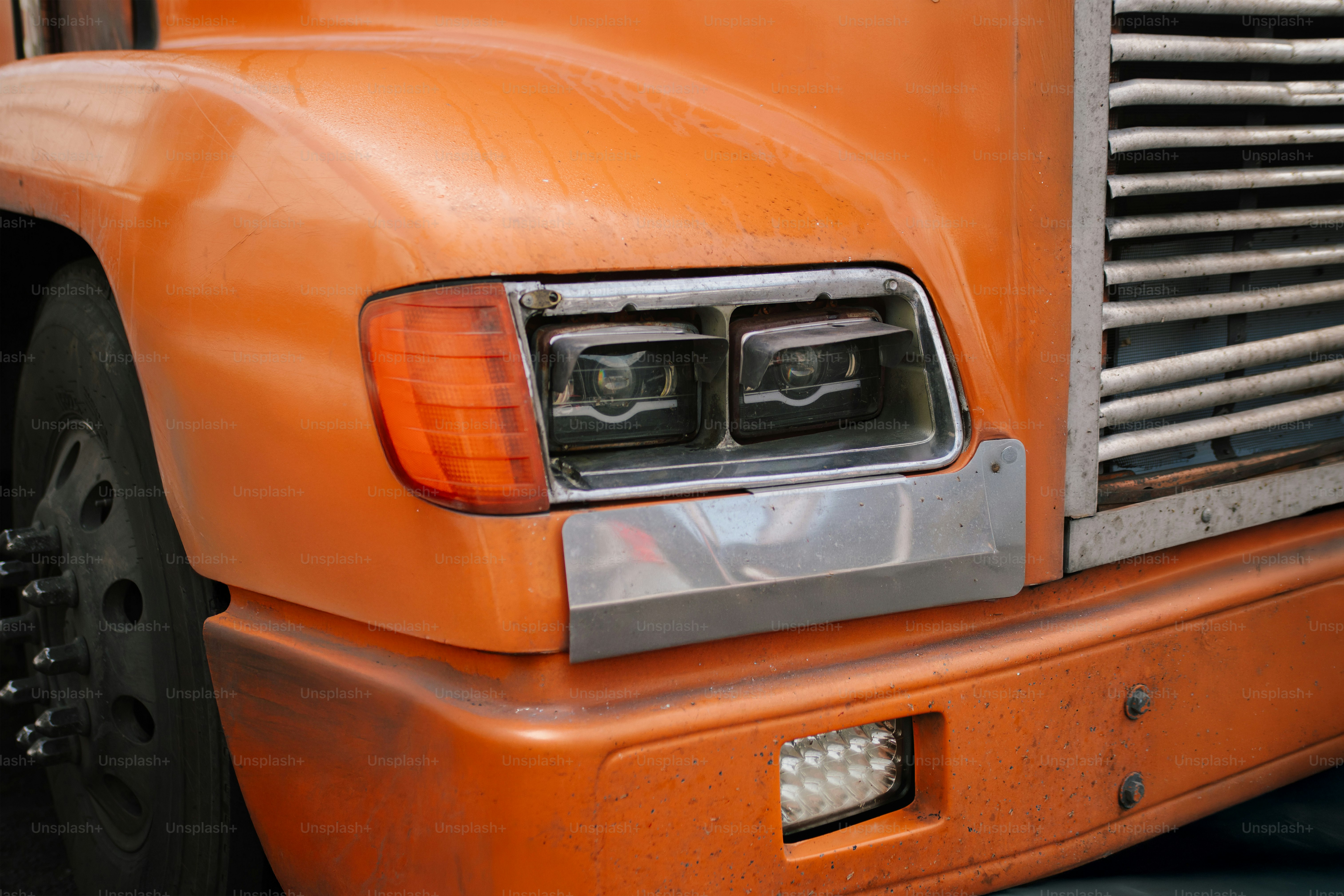 Close-up of an orange truck's headlight and grille