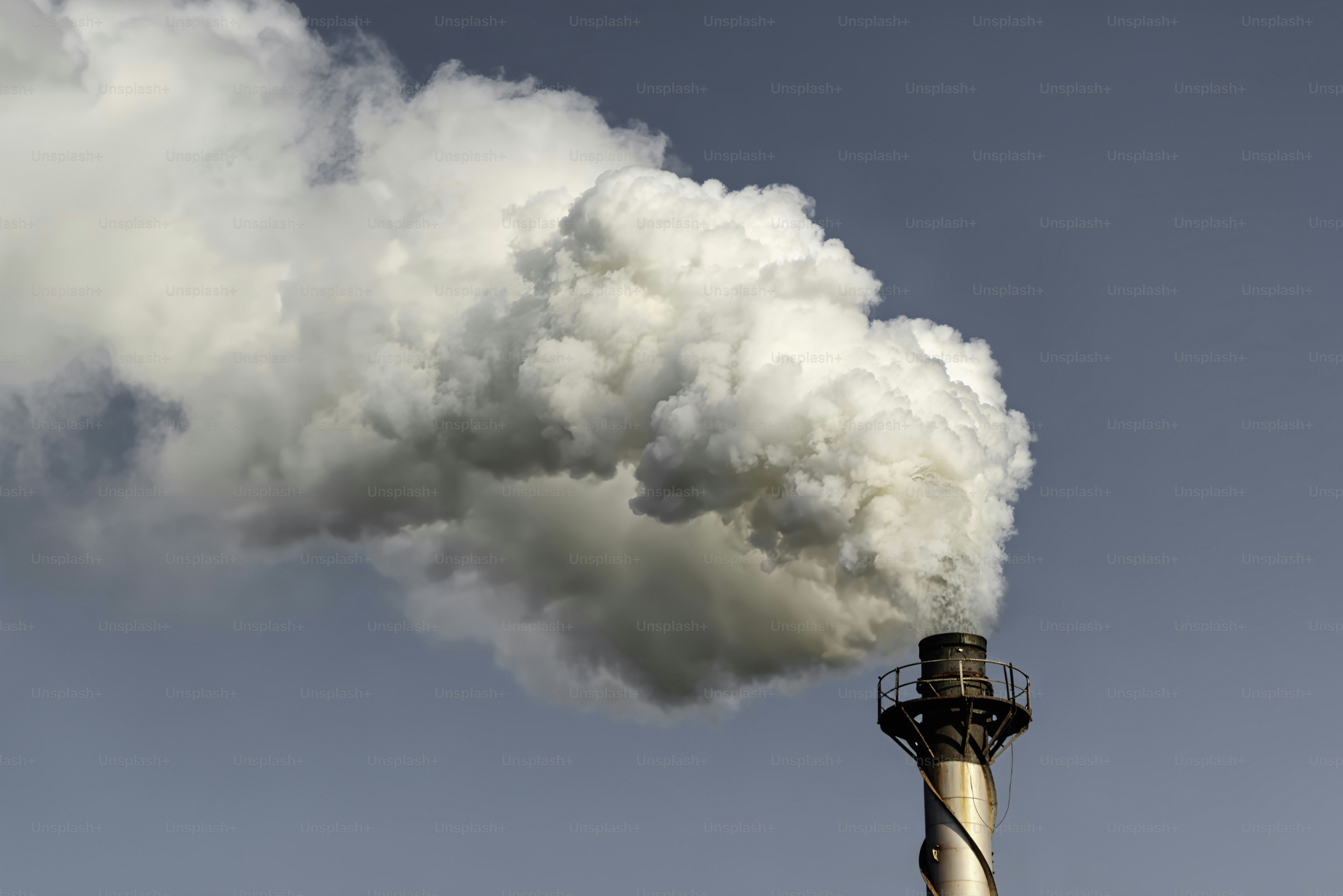Fumo che si alza da un camino industriale contro il cielo azzurro