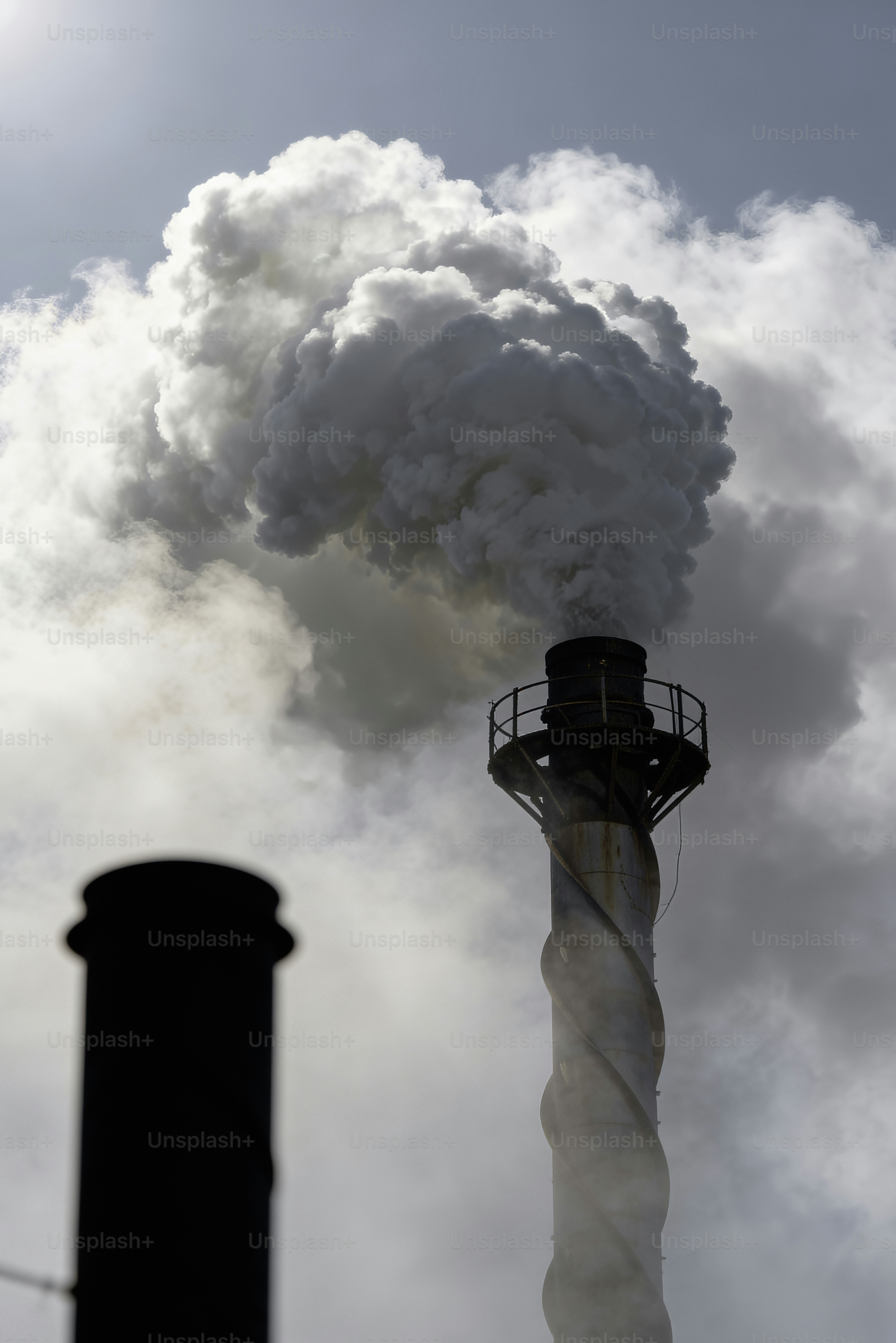 Il fumo si alza dai camini industriali contro un cielo nuvoloso.