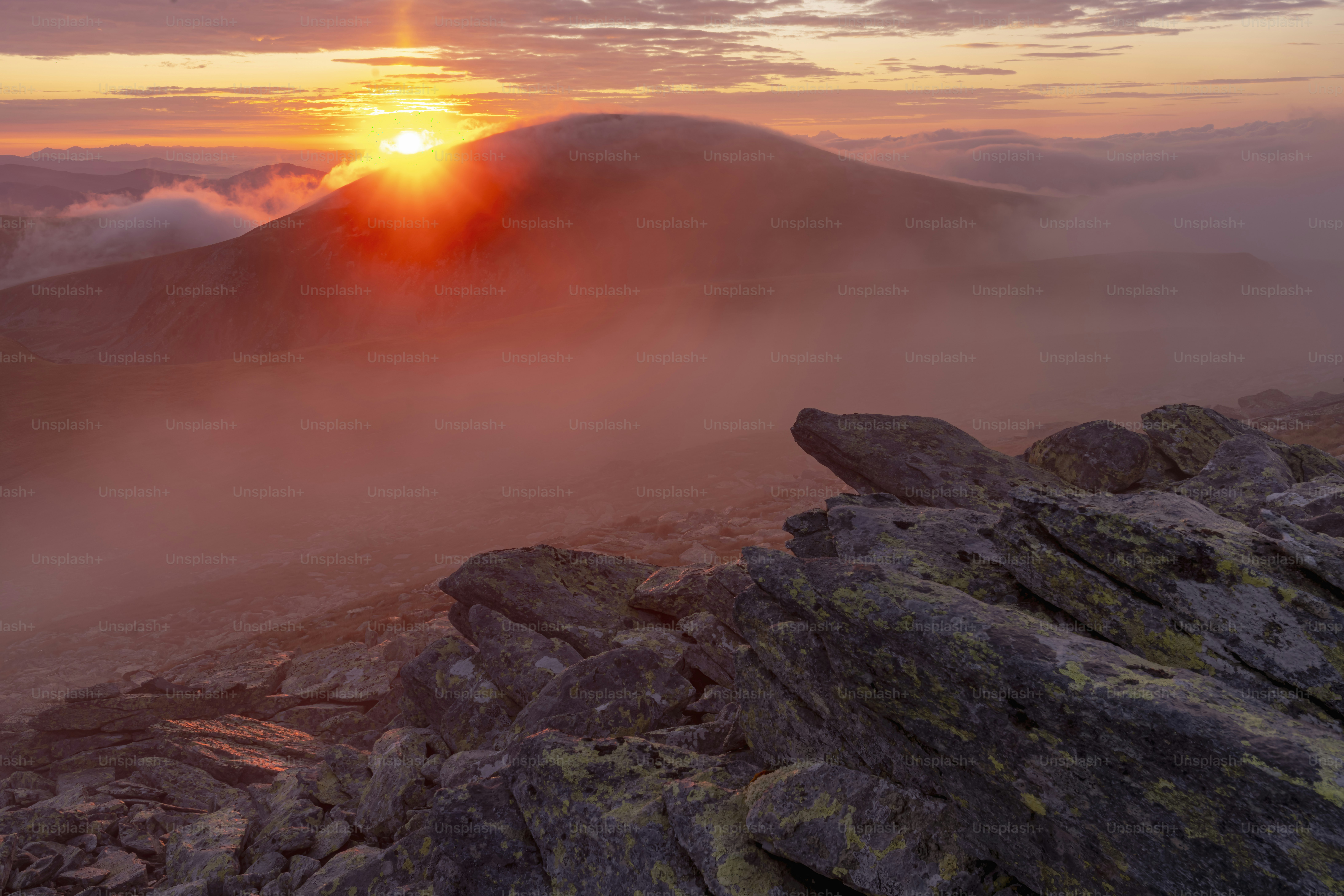 L'alba su una cima montuosa nebbiosa con un primo piano roccioso