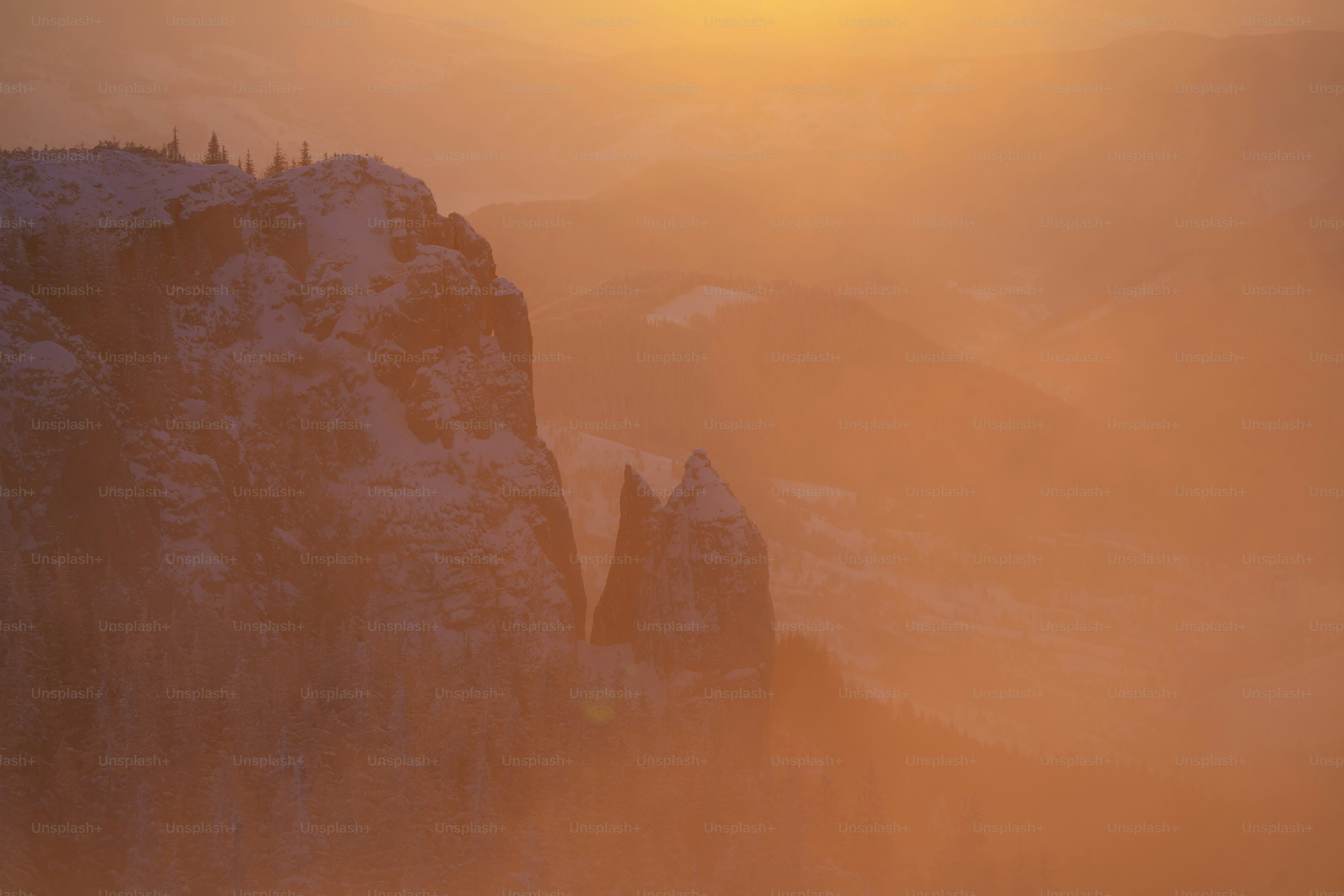 Cime innevate avvolte da una nebbia arancione all'alba.