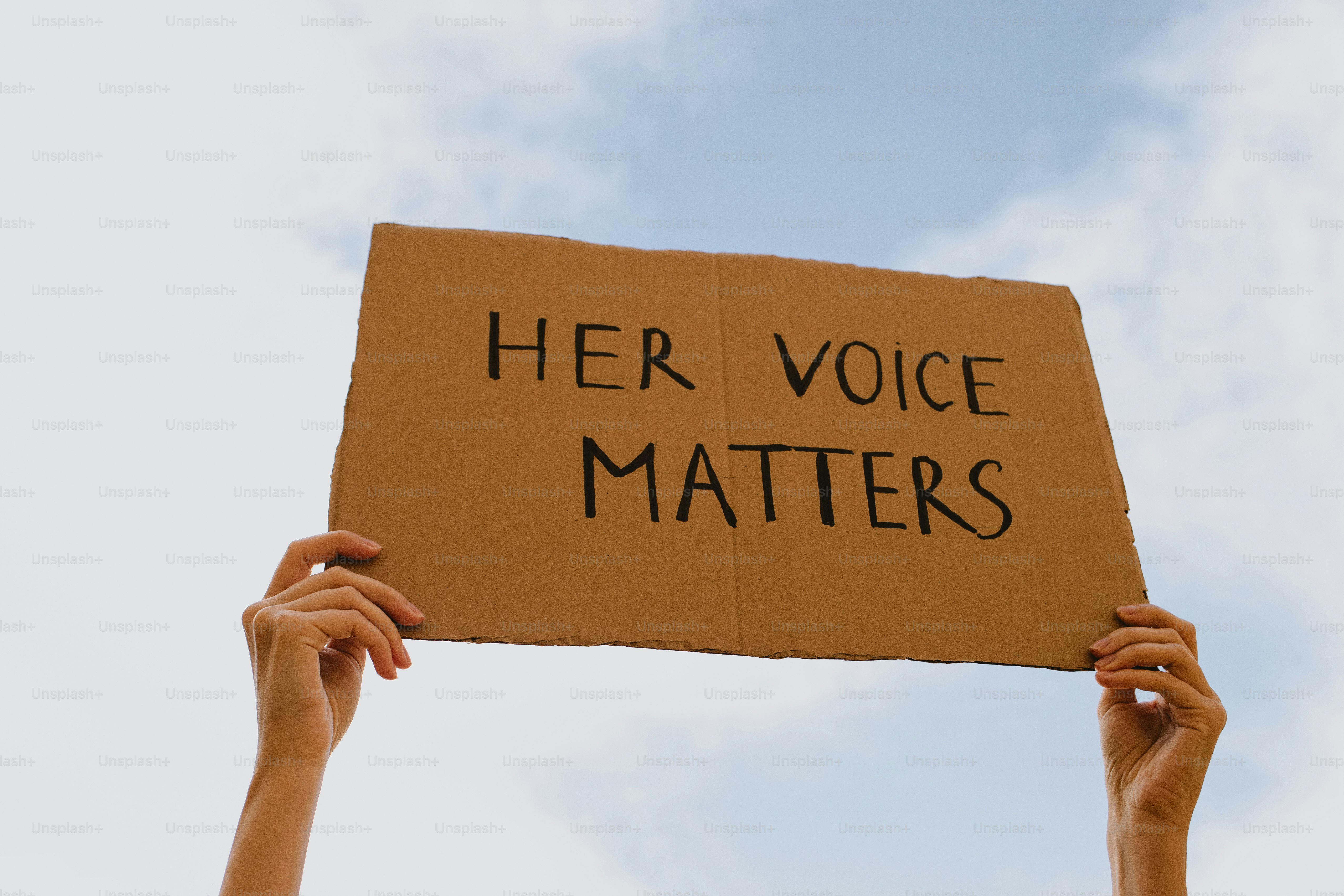 Hands holding a sign that says her voice matters