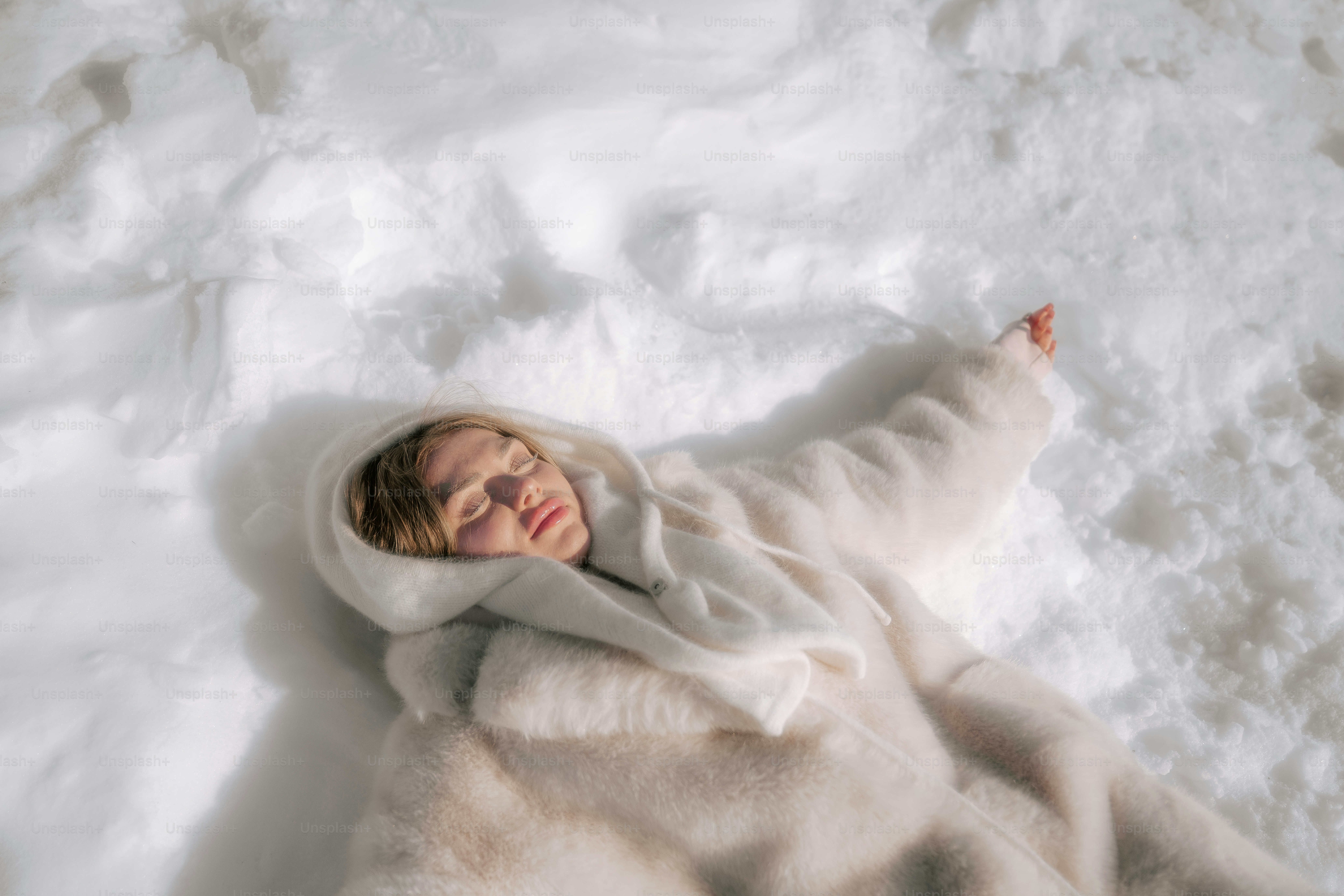 A woman in a white coat lies in the snow