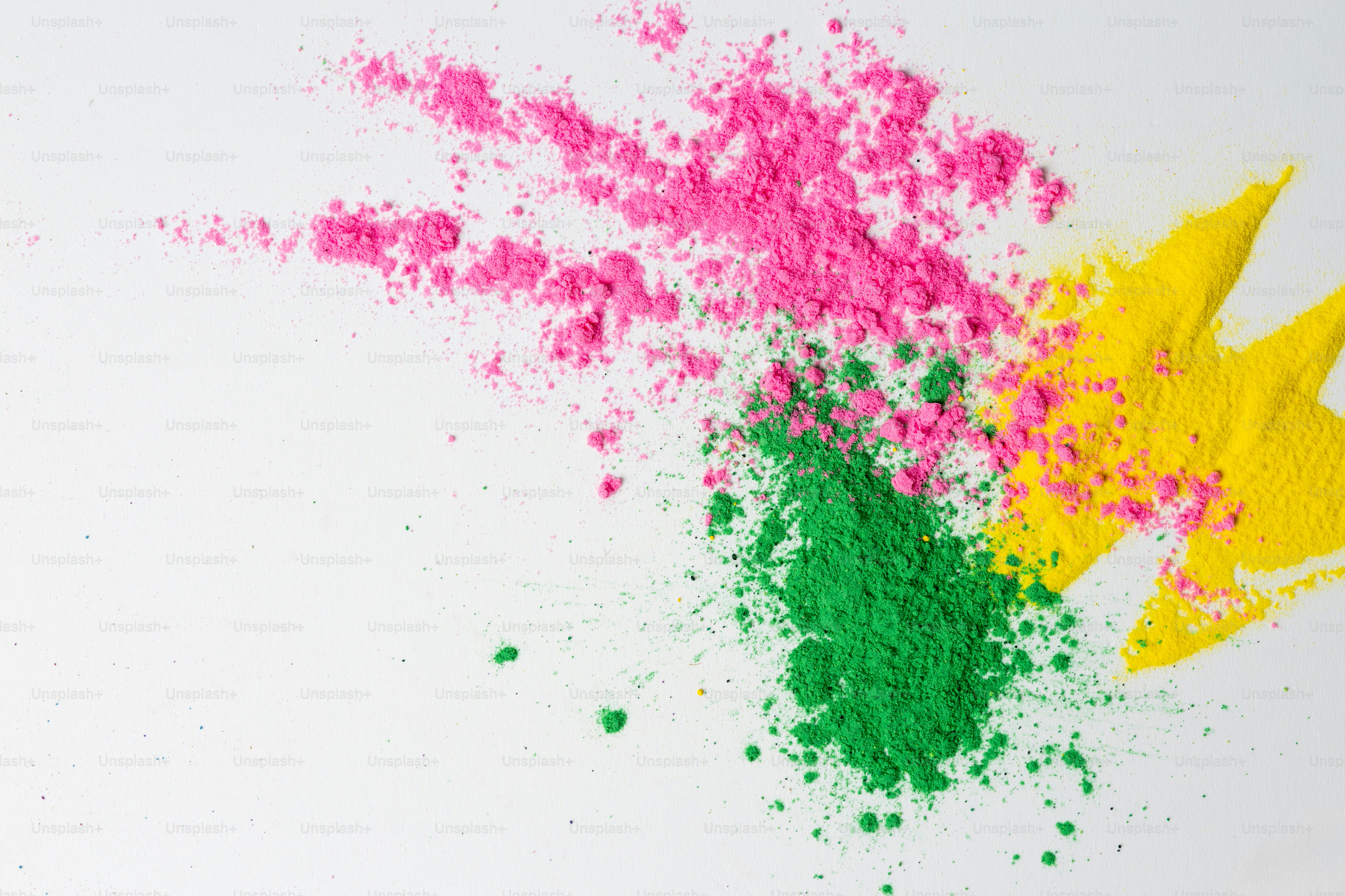 Pink, green, and yellow powder scattered on white background