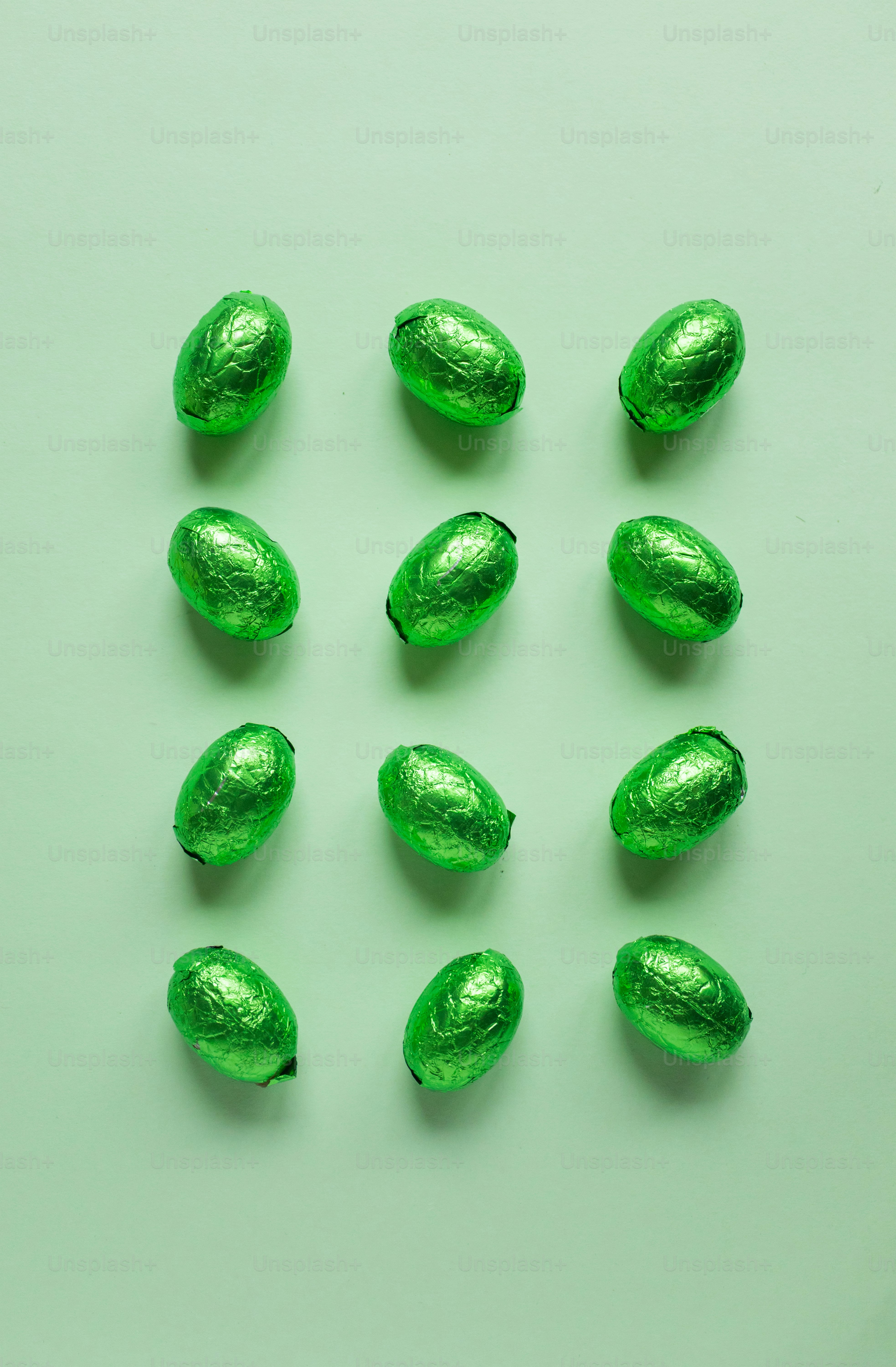 Doce huevos de chocolate envueltos en papel de aluminio verde dispuestos en una cuadrícula.
