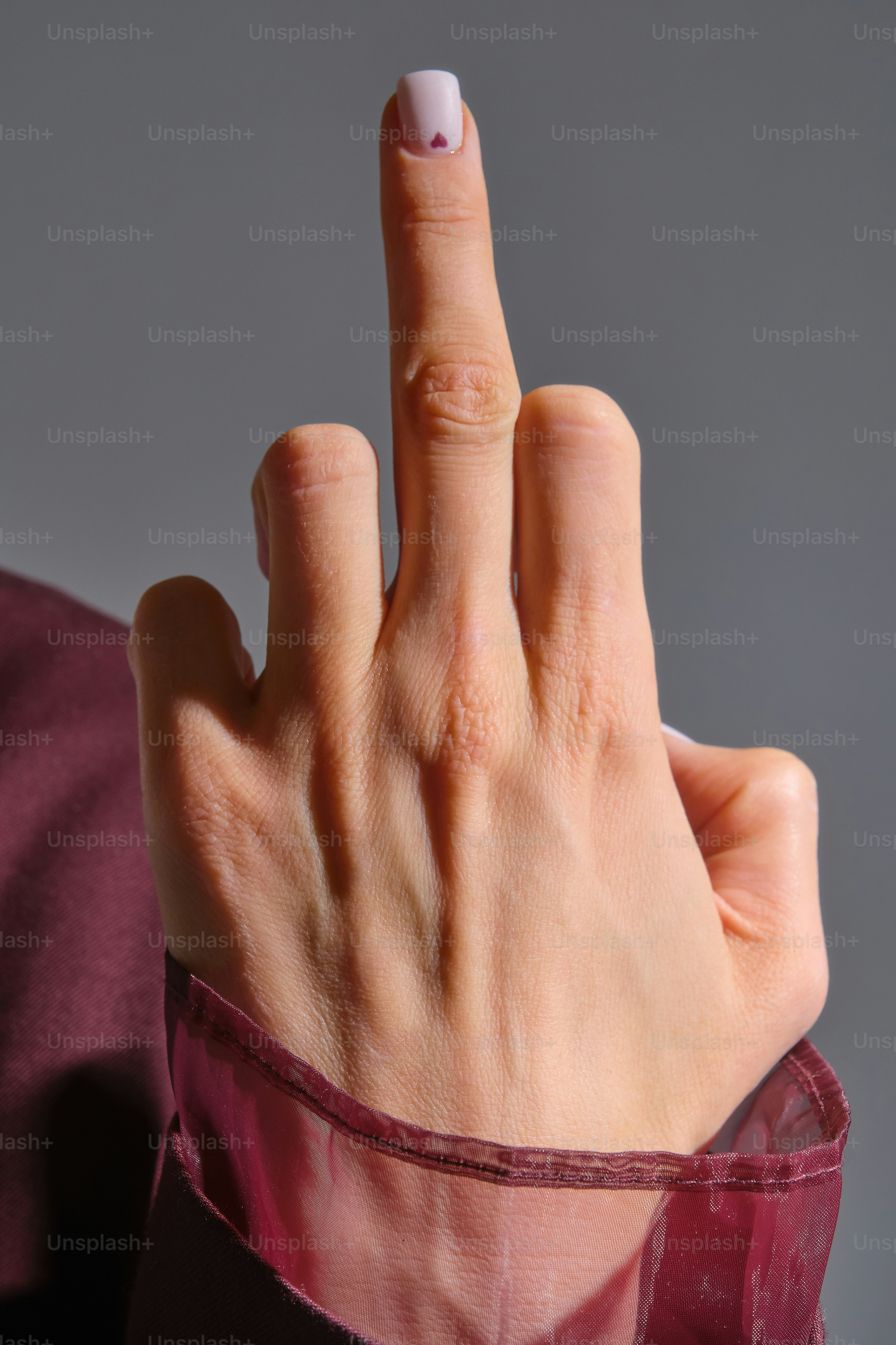 Eine Hand zeigt mit lackierten Nägeln auf den Mittelfinger.