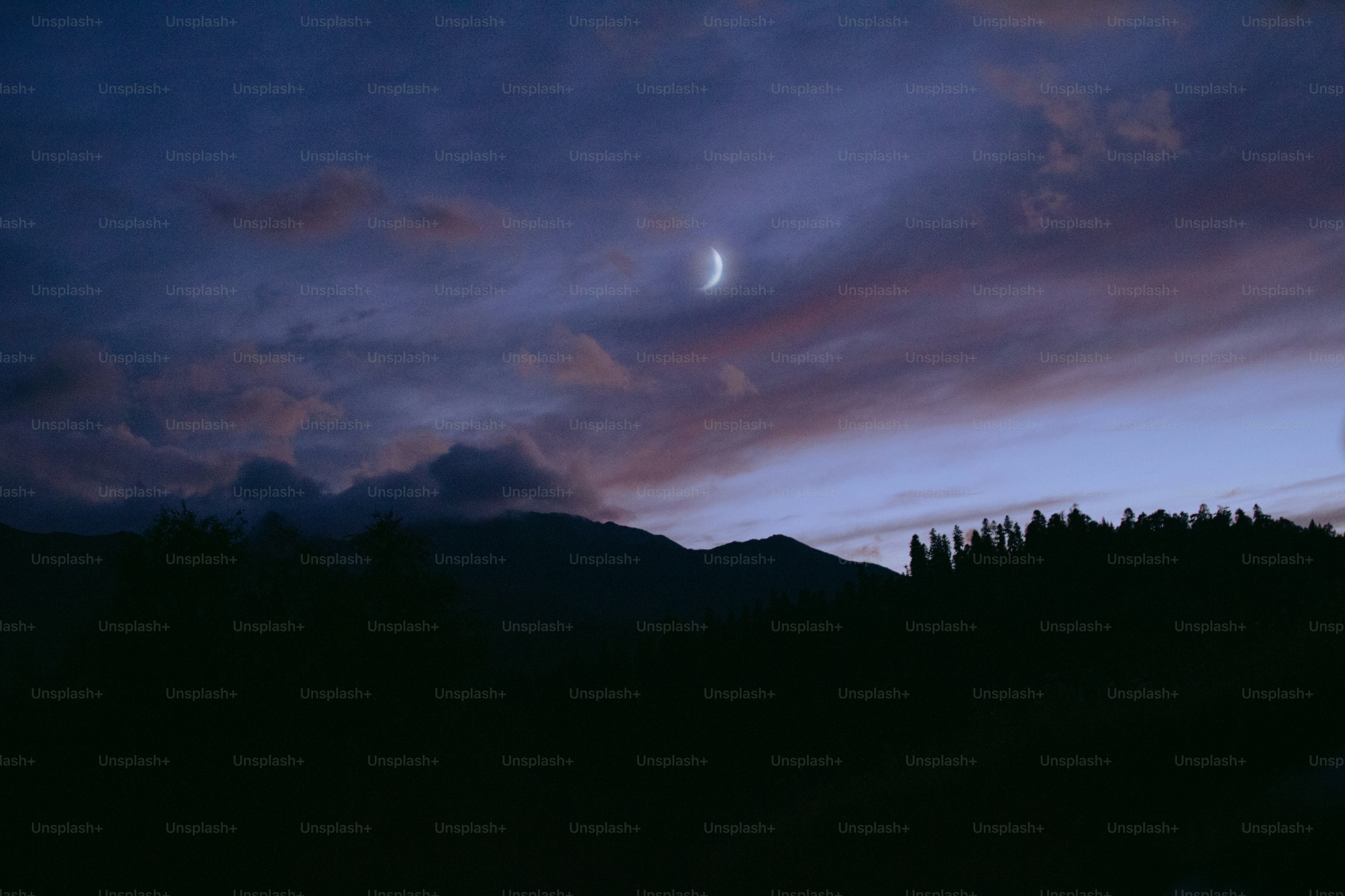Crescent moon in a twilight sky over mountains.
