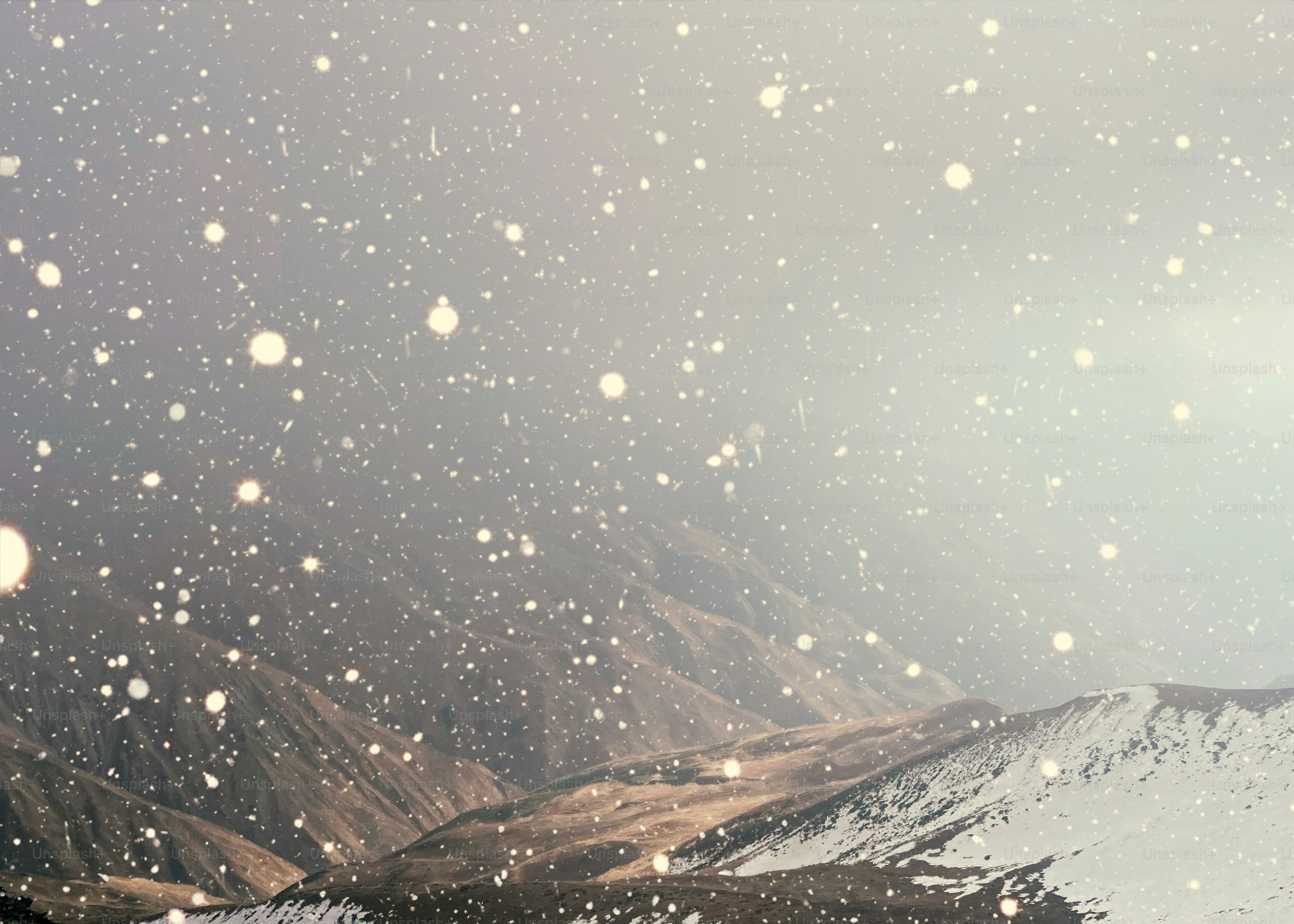 Snow falling over a mountainous landscape.