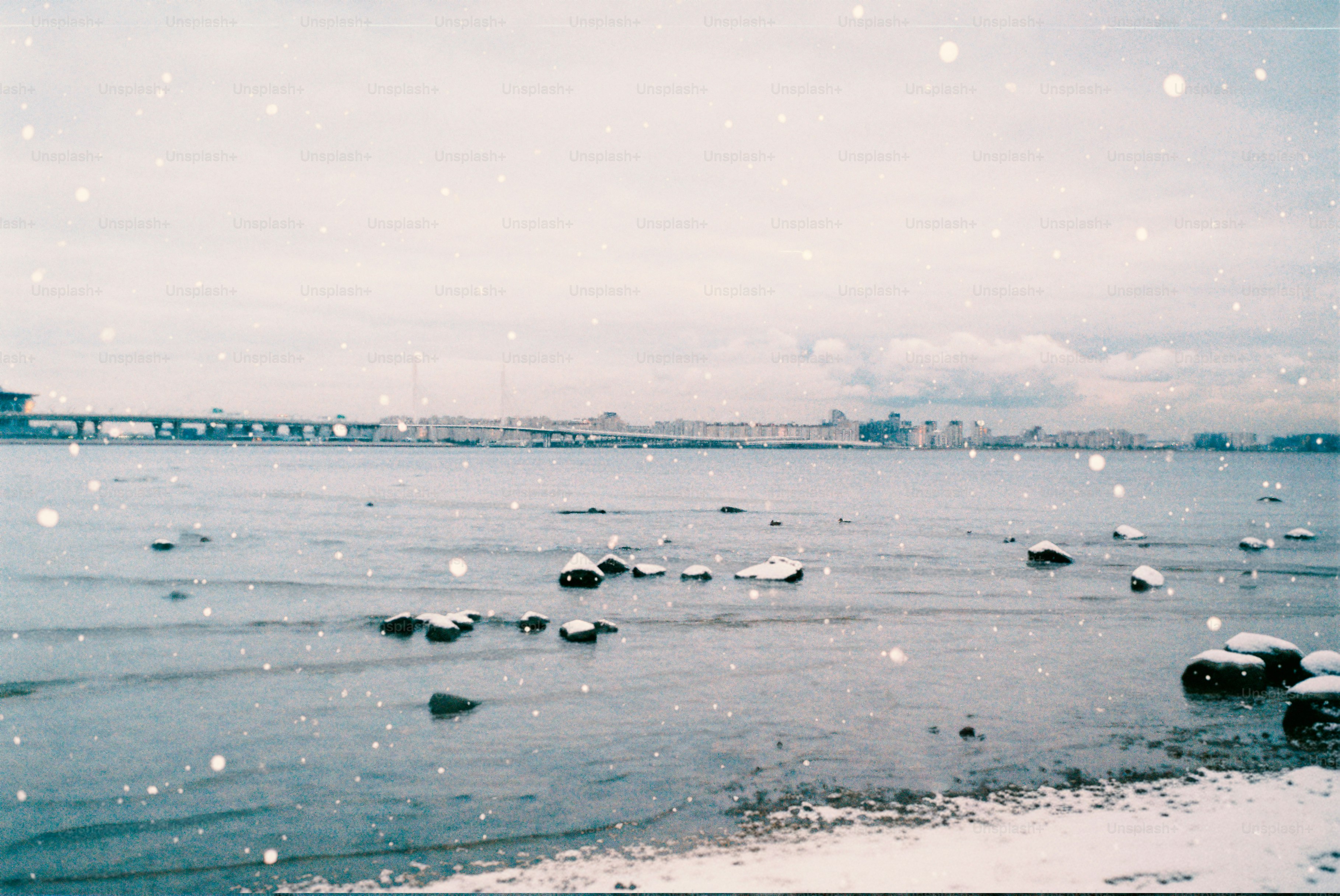 Snow falls on a frozen lake with distant city skyline.