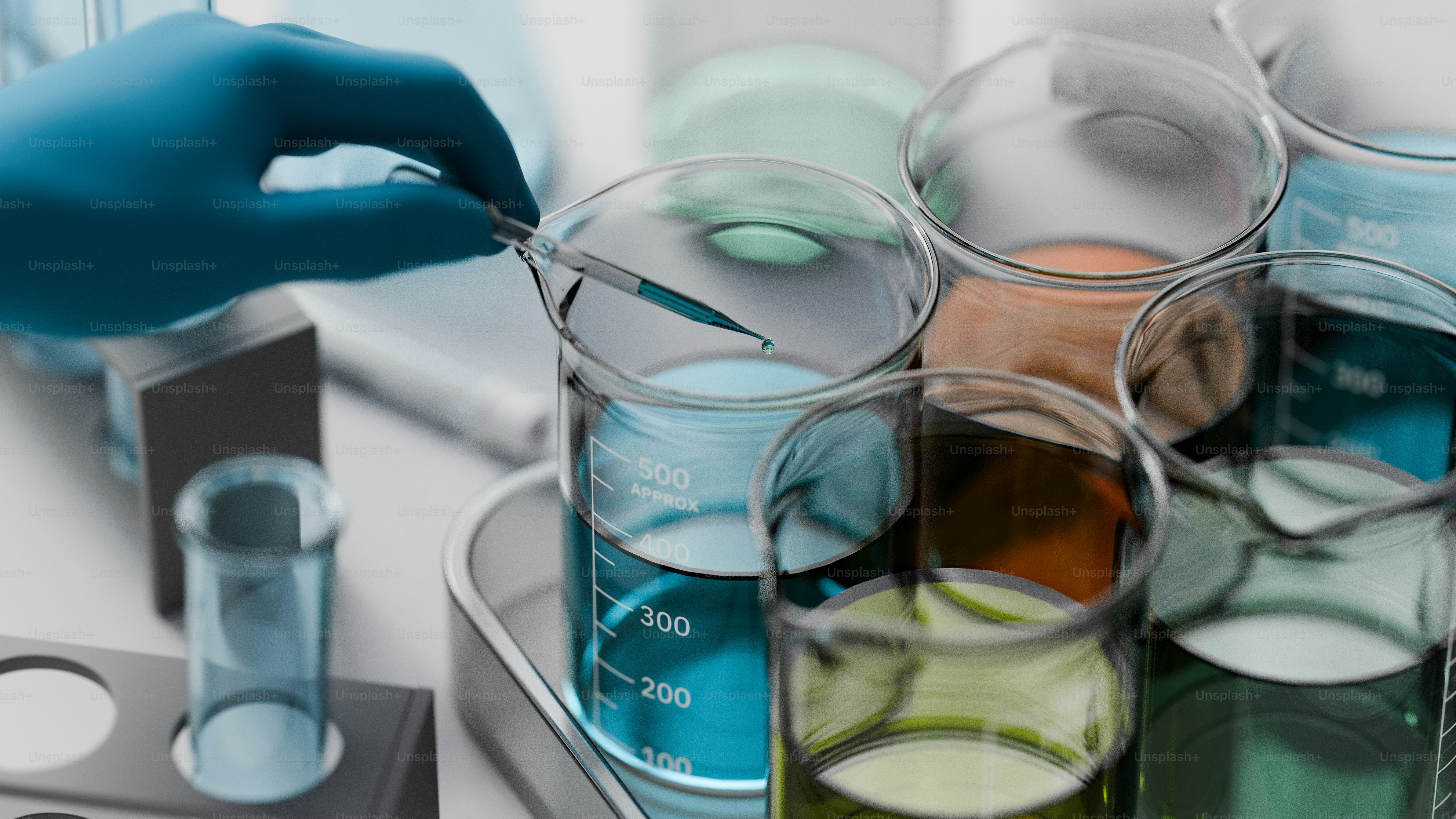 La mano guantata lascia cadere il liquido nel becher con becher colorati