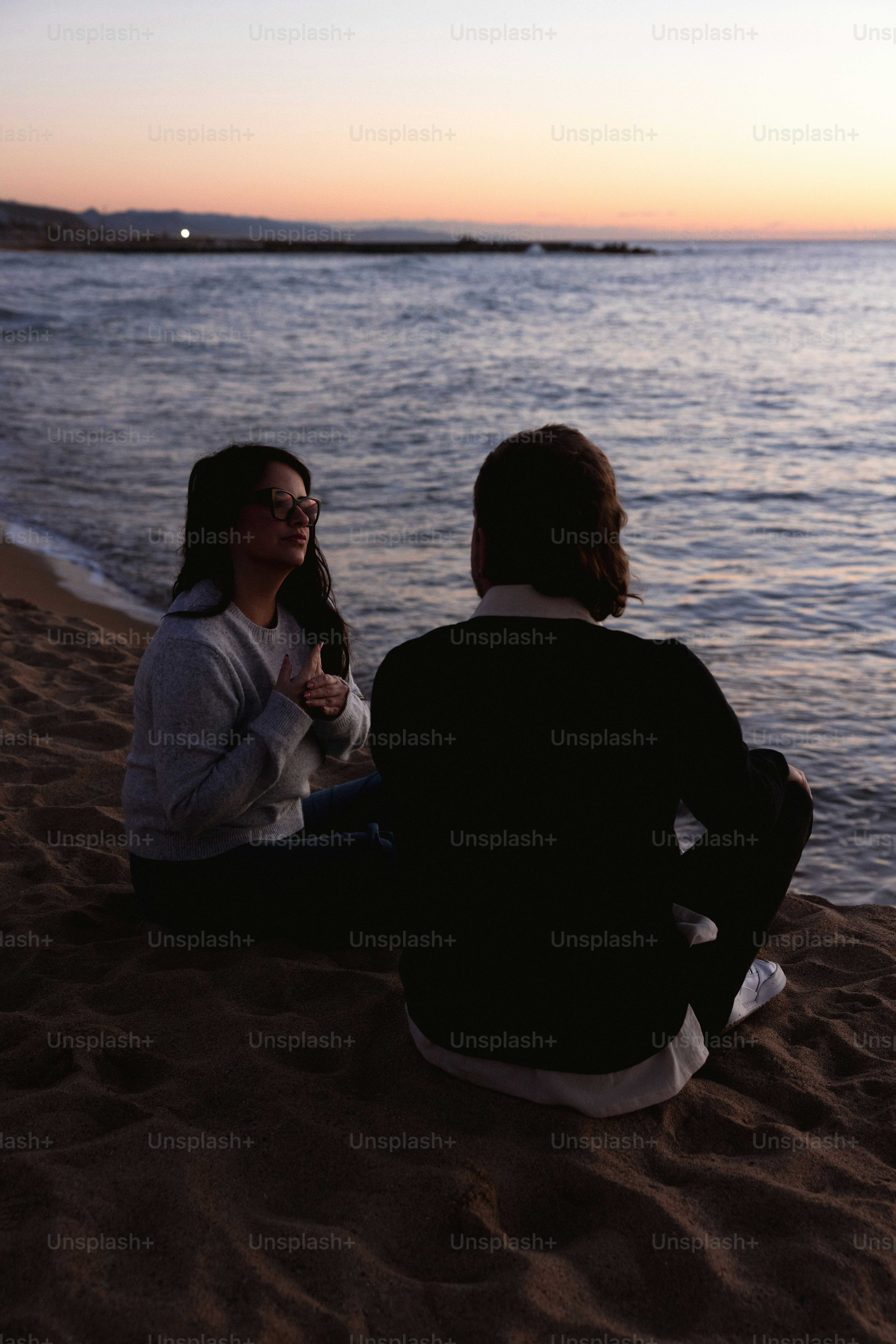 Deux personnes assises sur une plage au coucher du soleil.