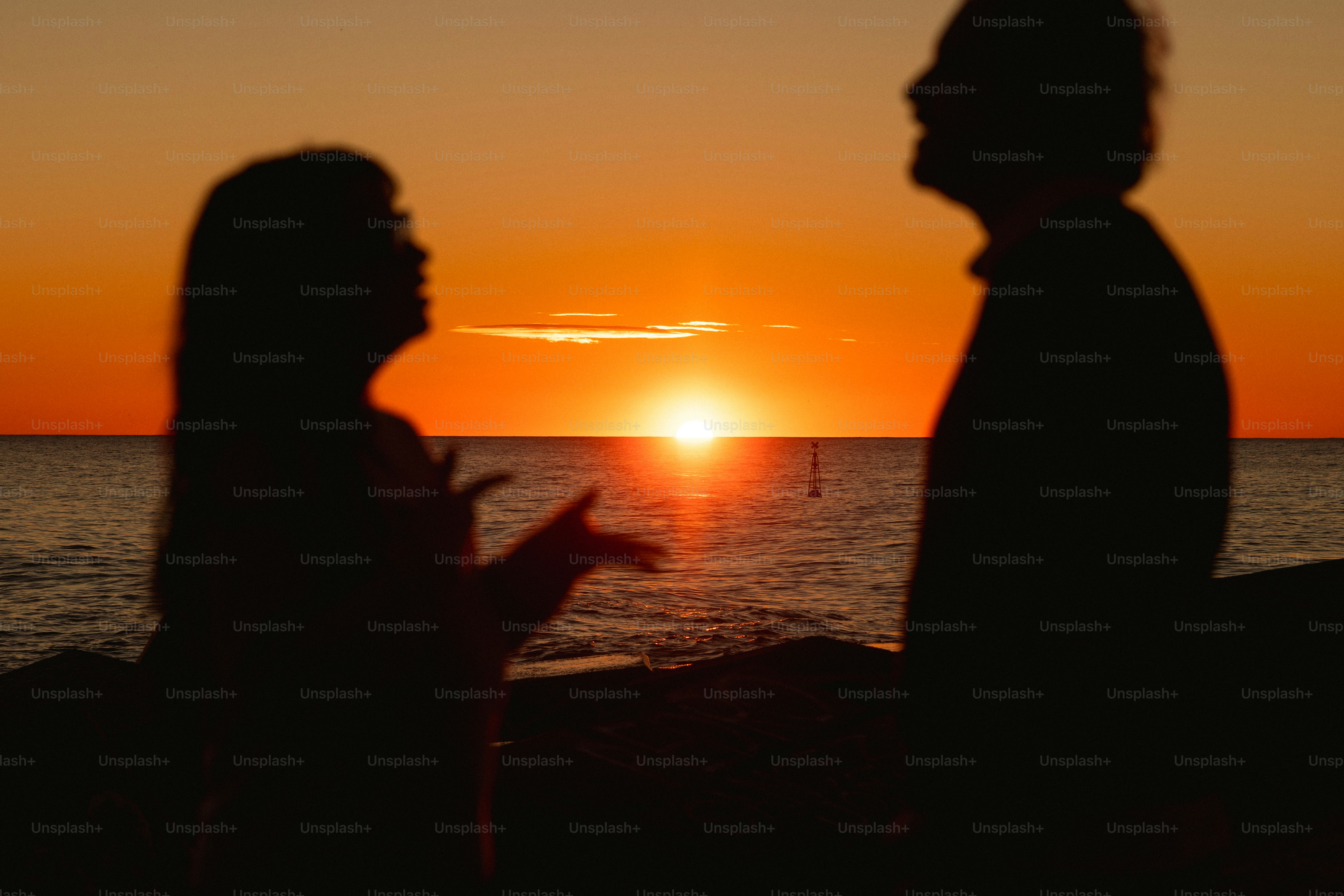 Silhouettes de deux personnes parlant au coucher du soleil au bord de l’océan
