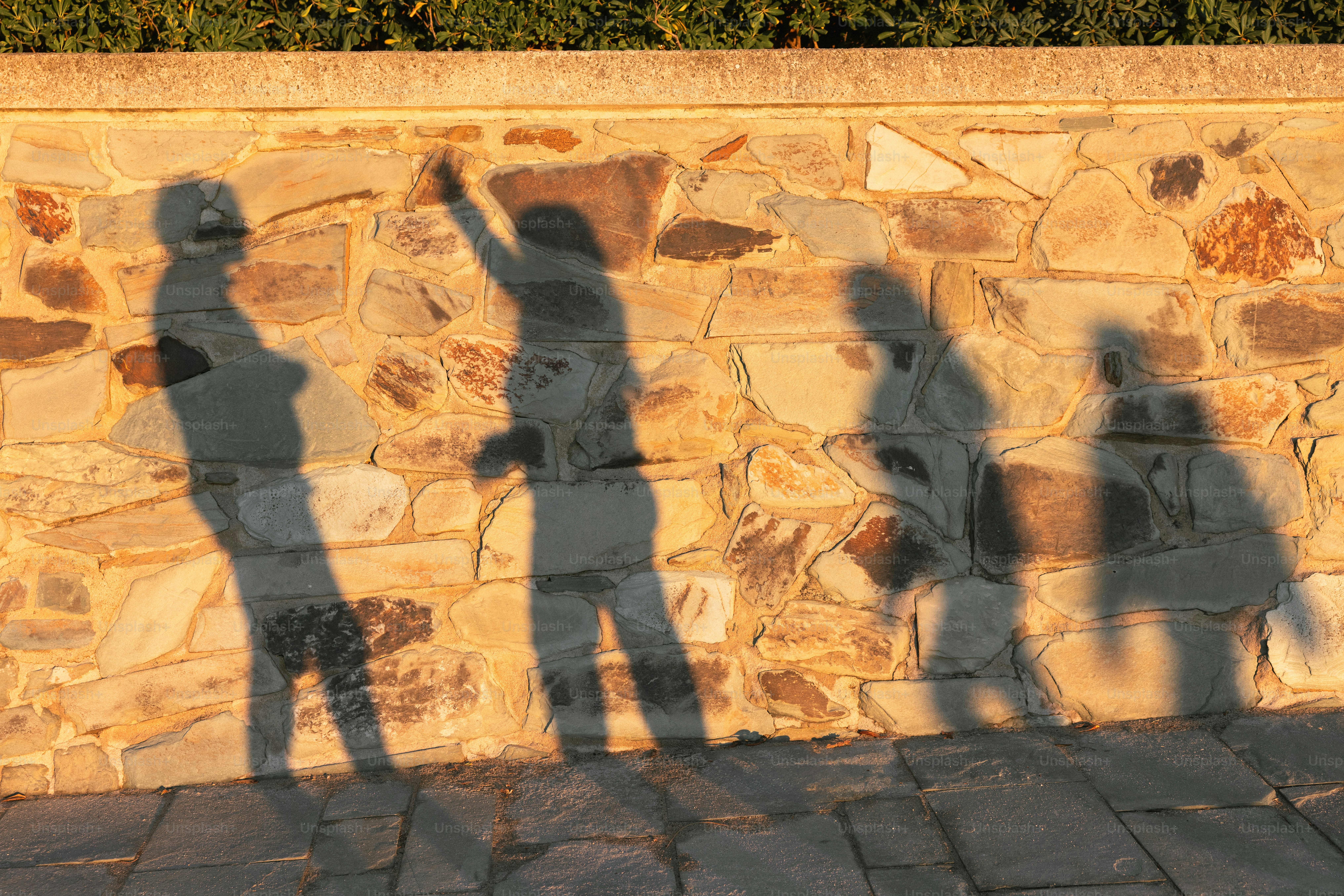 Schatten von vier Personen auf einer Steinmauer.