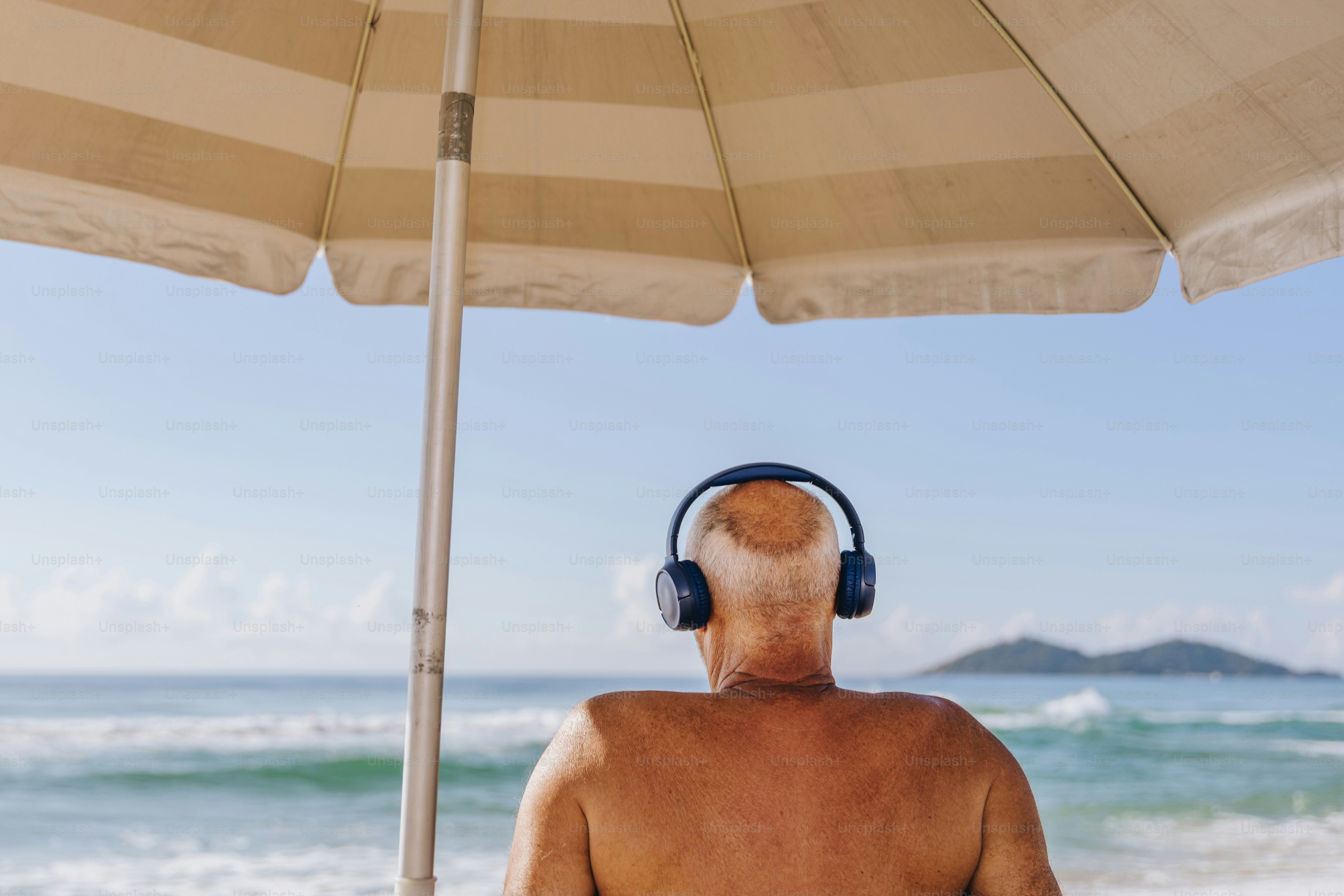 Man with headphones under beach umbrella listening to music